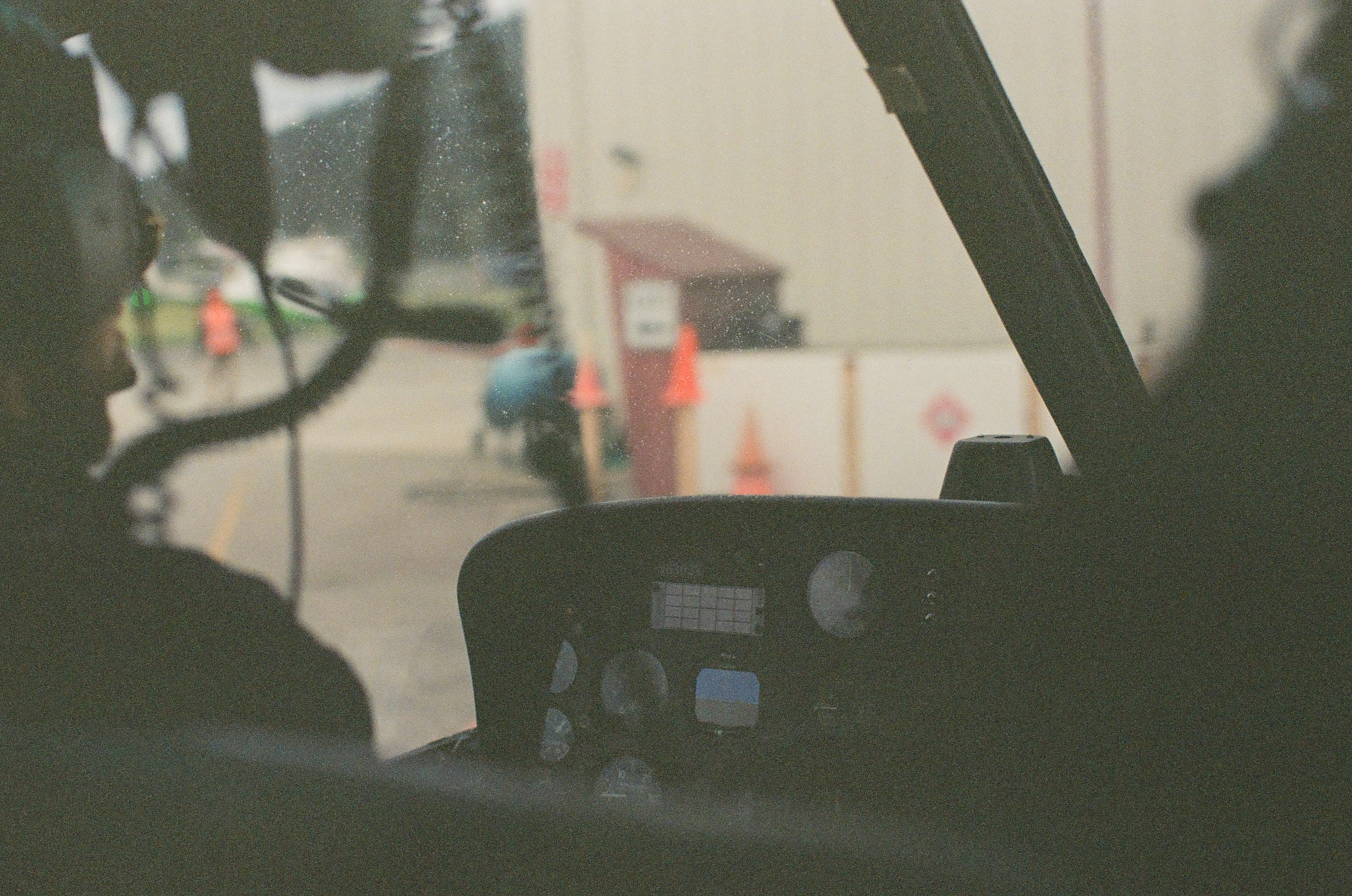 Dark aircraft controls frame a bright airfield where small figures and orange cones stand beyond the windshield.