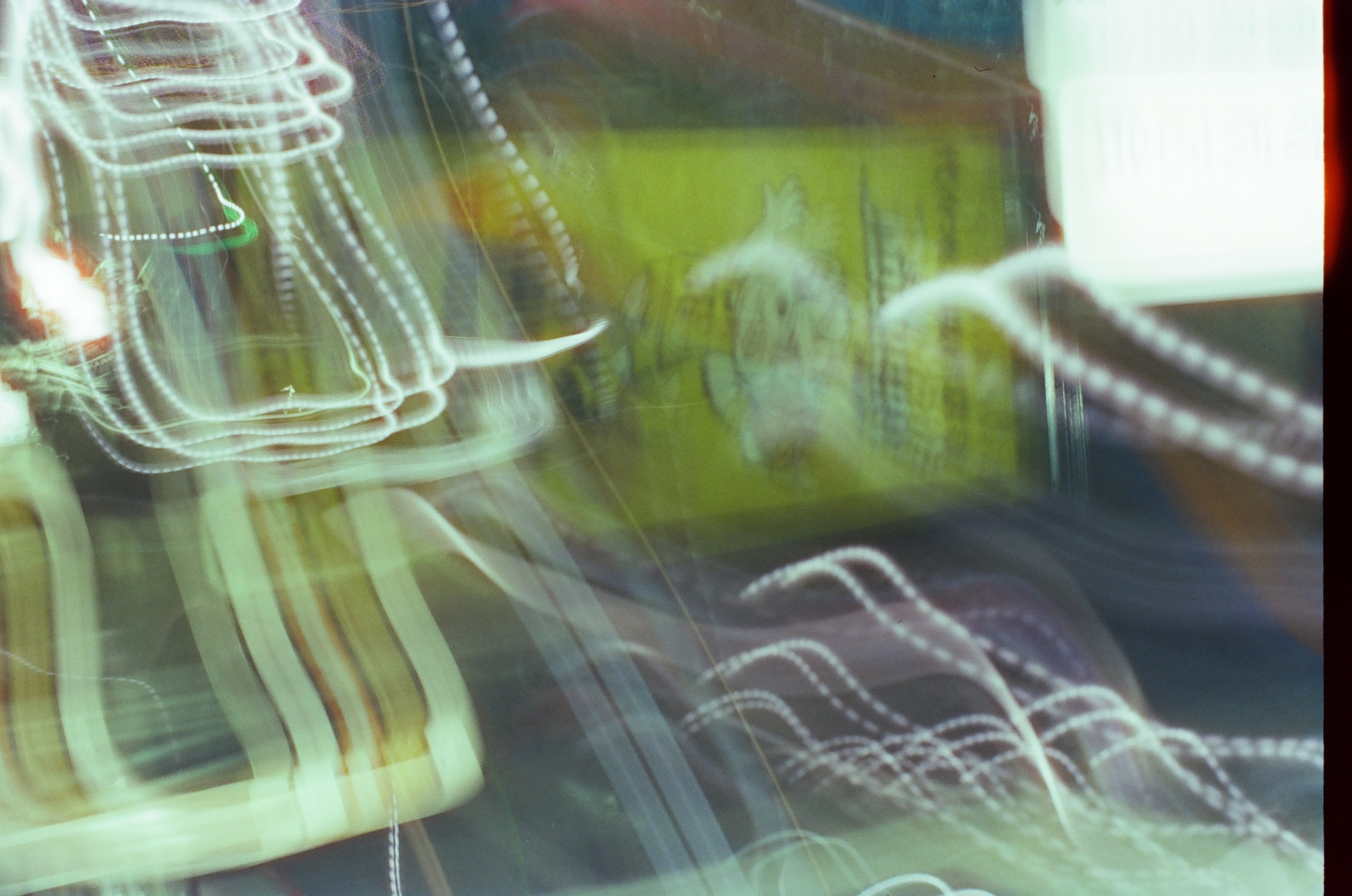 Looping strands of white light trail across the frame over a dim yellow poster bearing an indistinct illustrated figure and unreadable text.