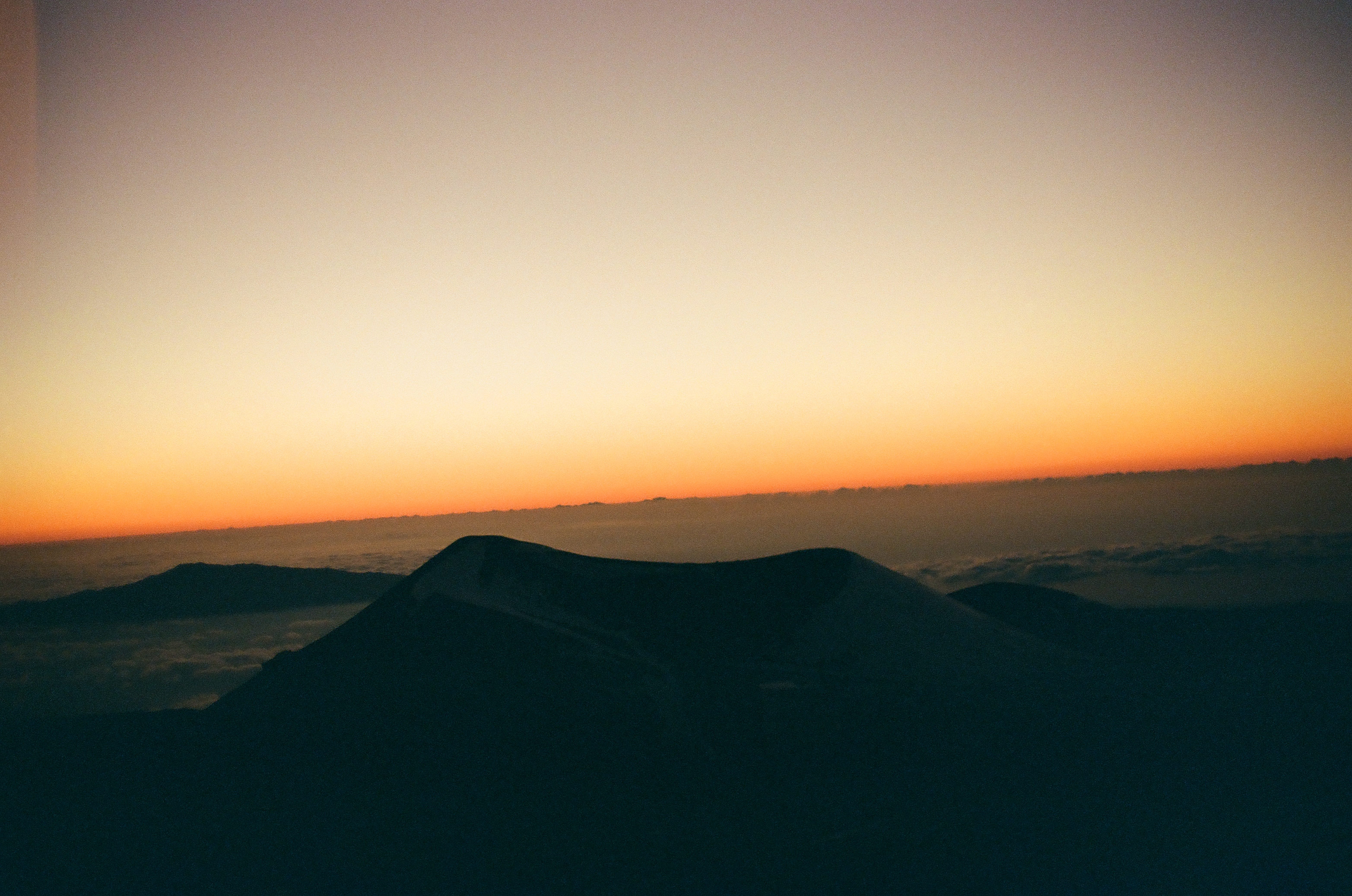 A thin orange afterglow spans the horizon beyond several dark rounded cones and distant layered land.