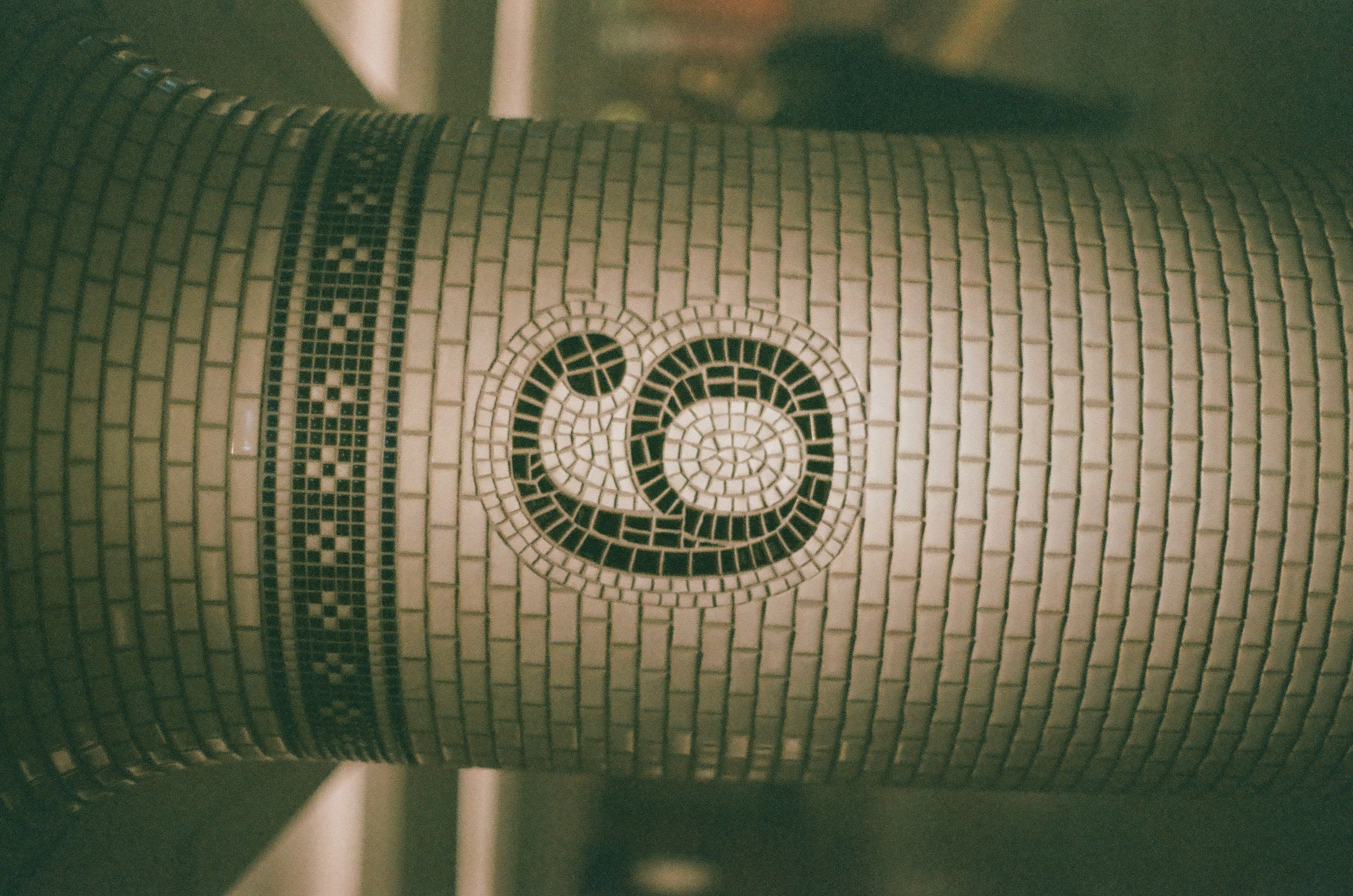 The mosaic numeral six sits at the center of a pale curved tiled column under green light.