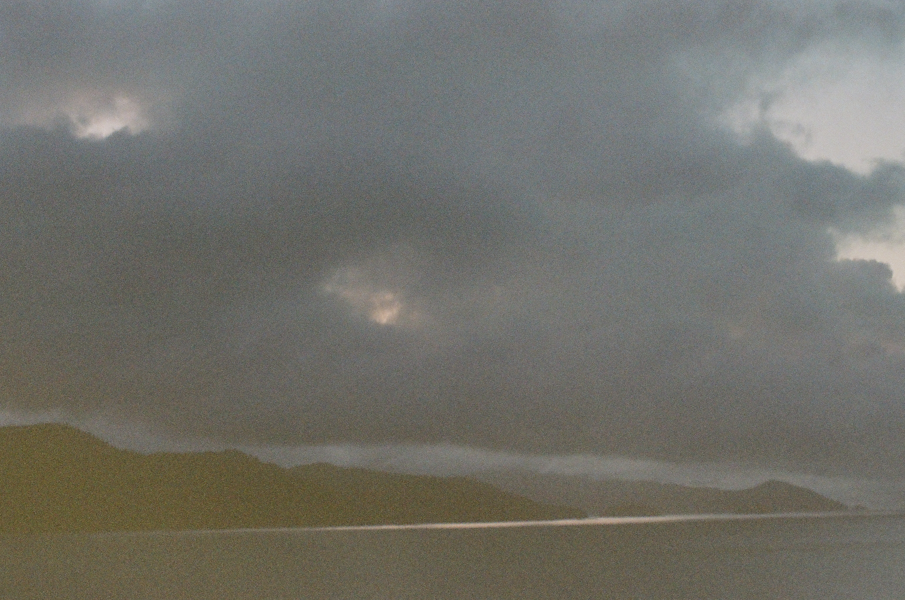 A rounded island silhouette sits beneath dense clouds pierced by several pale openings near the upper edge.