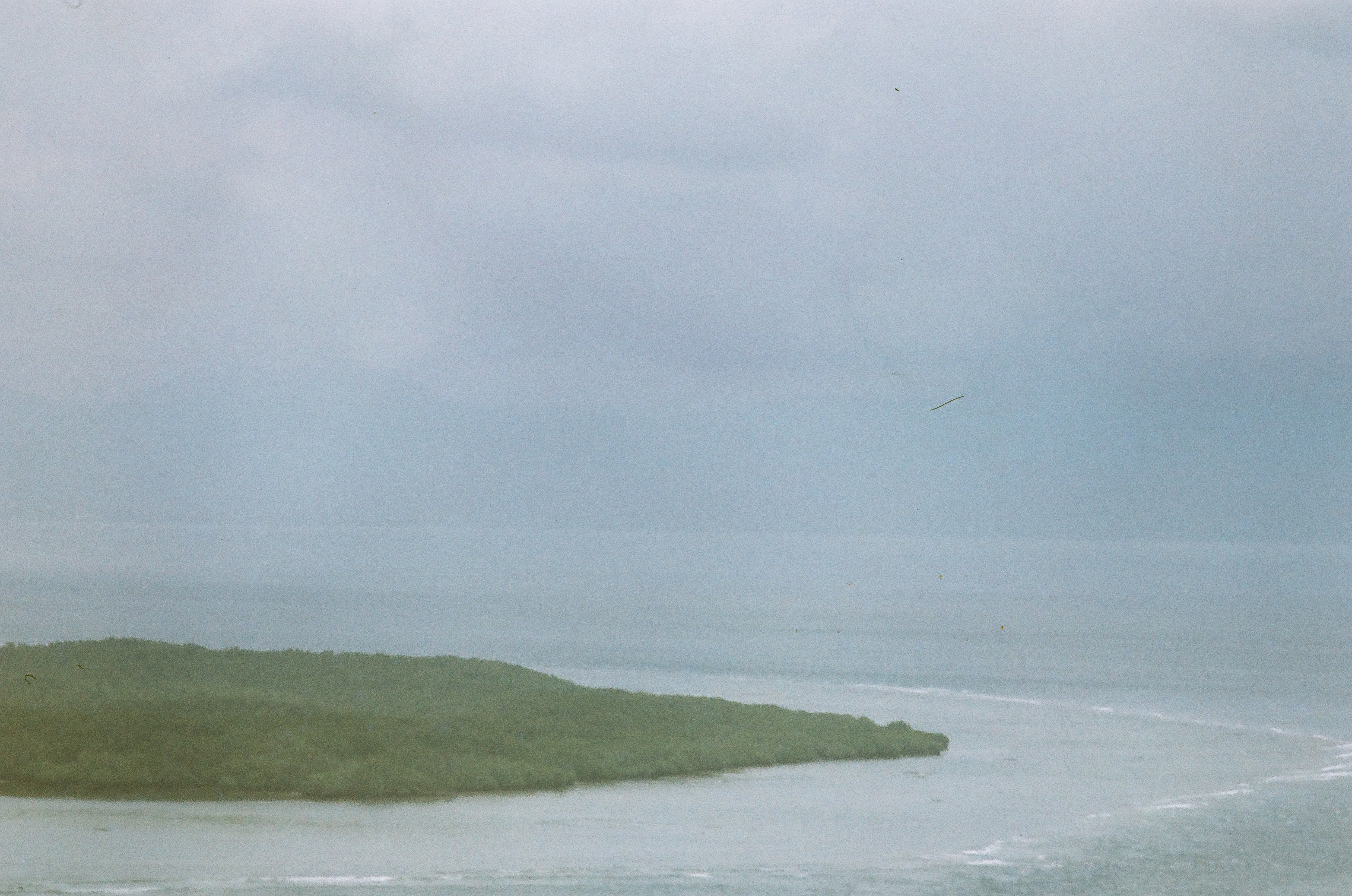 A low vegetated landmass extends into pale water beneath a hazy sky, with curved pale streaks visible far to the right.
