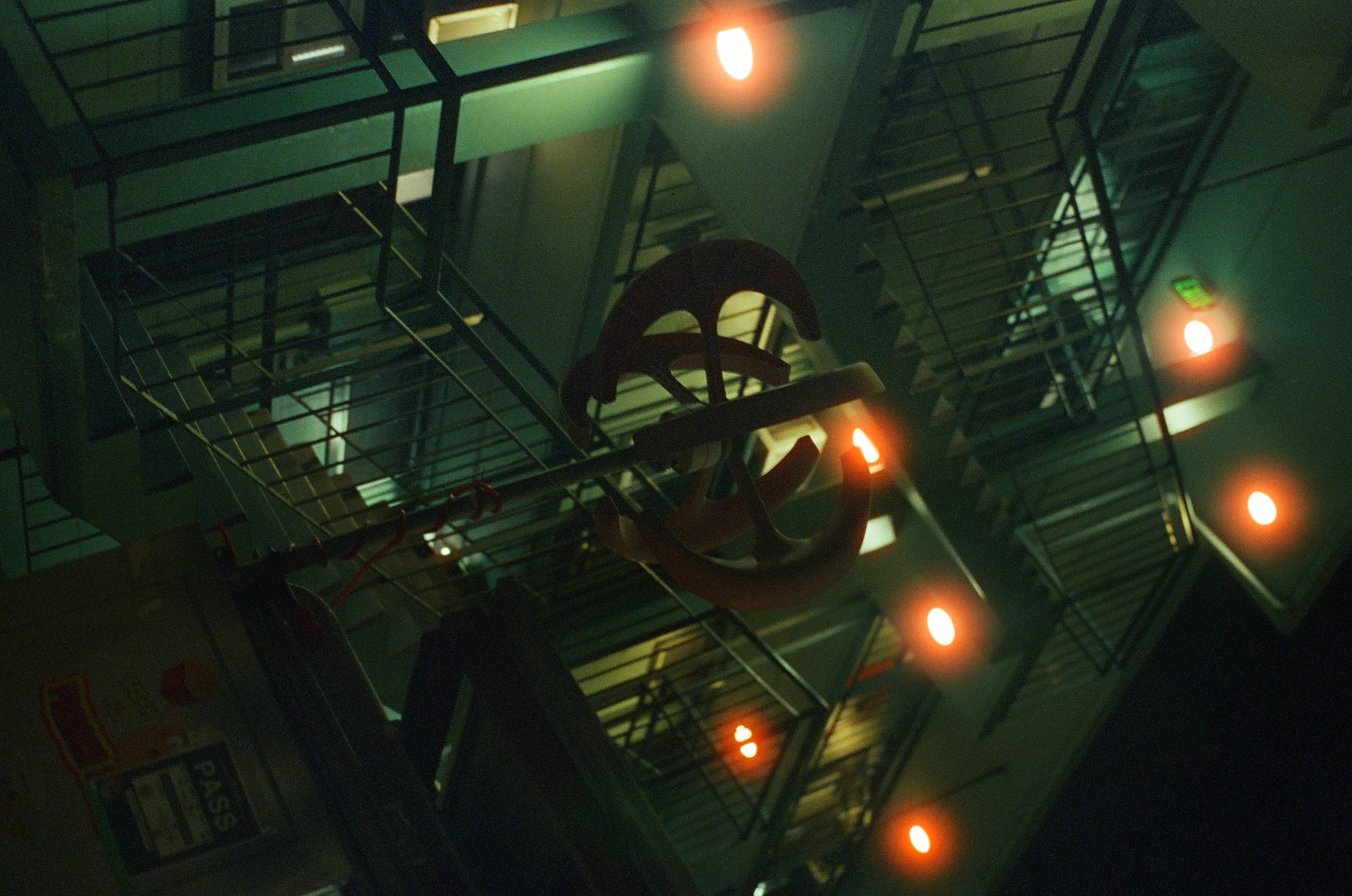 A geometric hanging fixture glows red and green above railings in a tall interior stairwell.