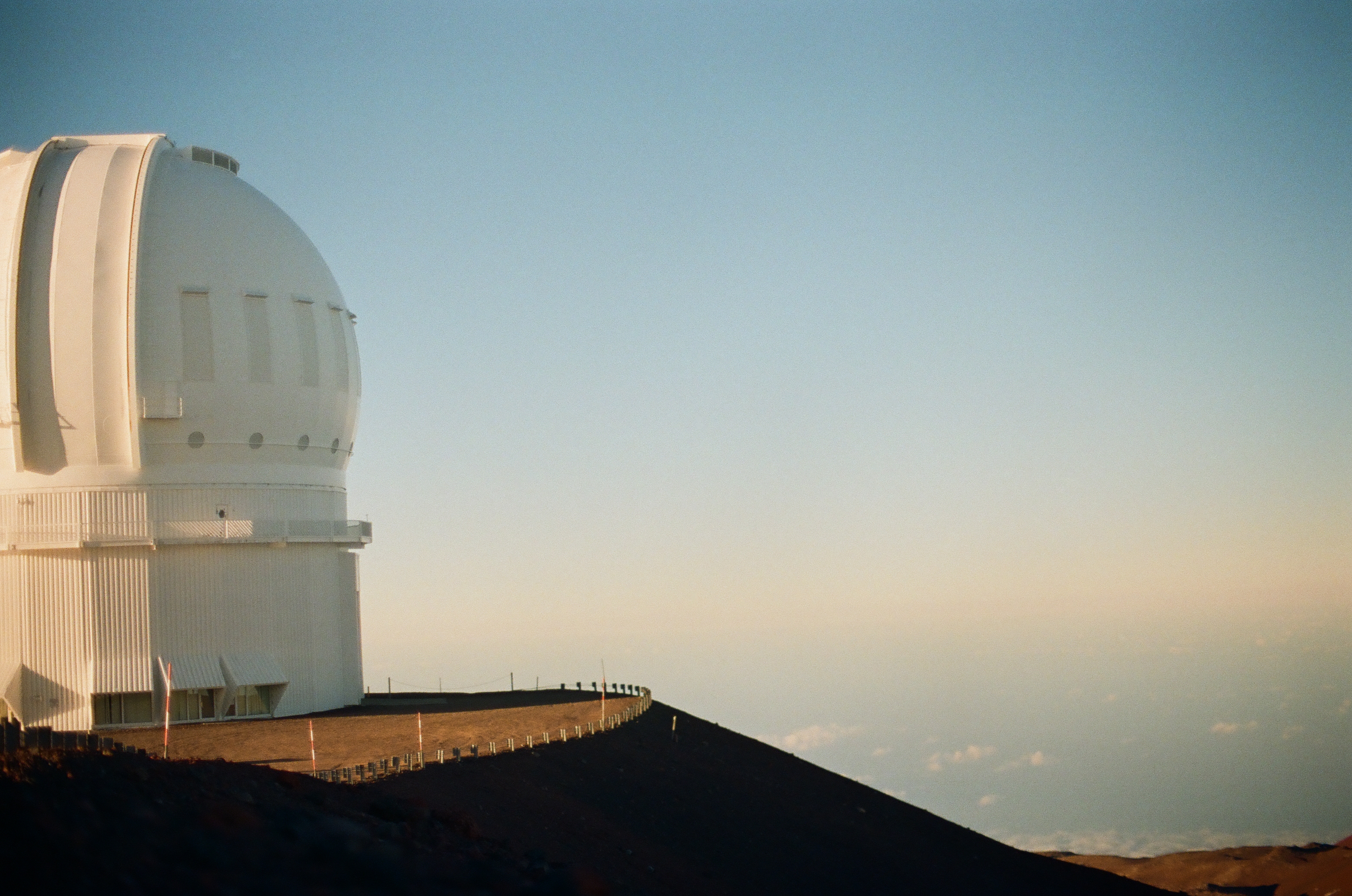 A large white observatory dome stands on a dark summit ridge beneath clear pale blue sky.