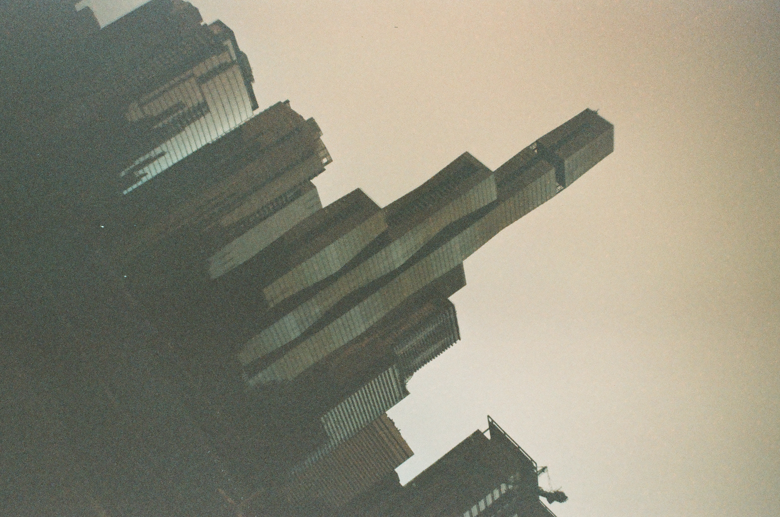 Several high-rise towers lean at a steep diagonal across a pale hazy sky, their vertical lines converging toward one upper corner.