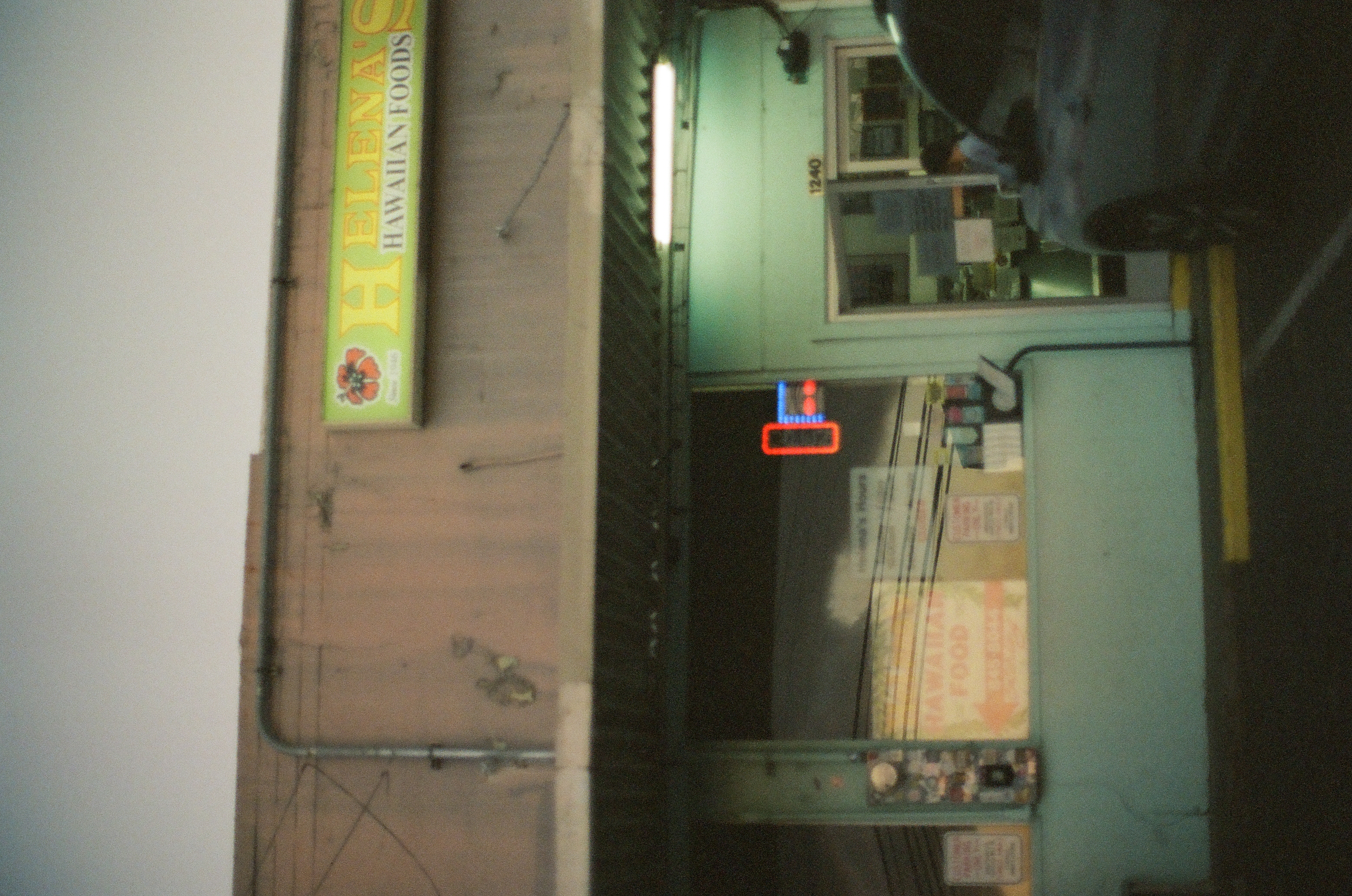 A low restaurant storefront sits behind parked vehicles with small signs clustered around its shaded entrance.