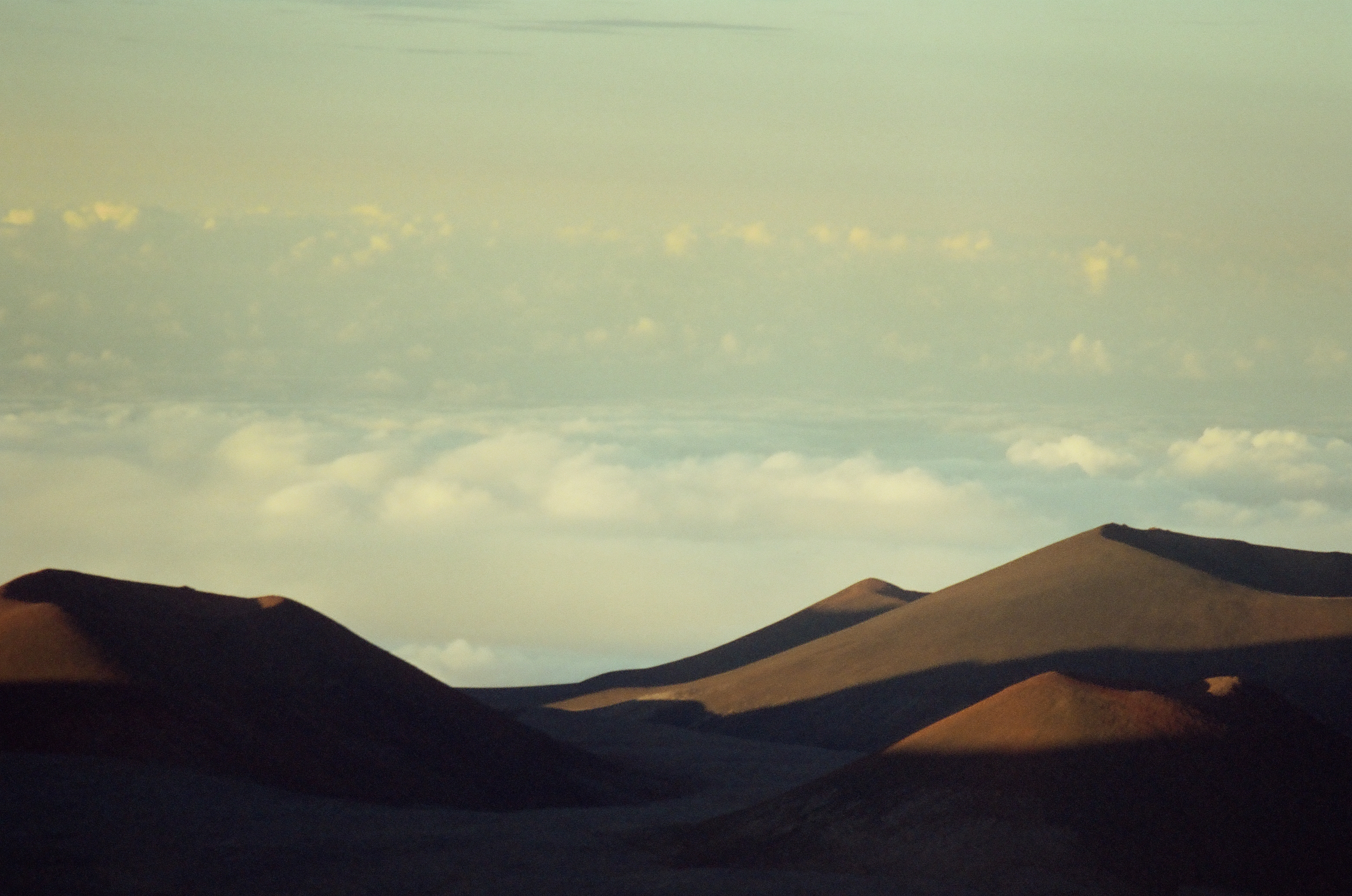 A sunlit brown ridge rises beyond deep shadow with a white cloud deck at the horizon.