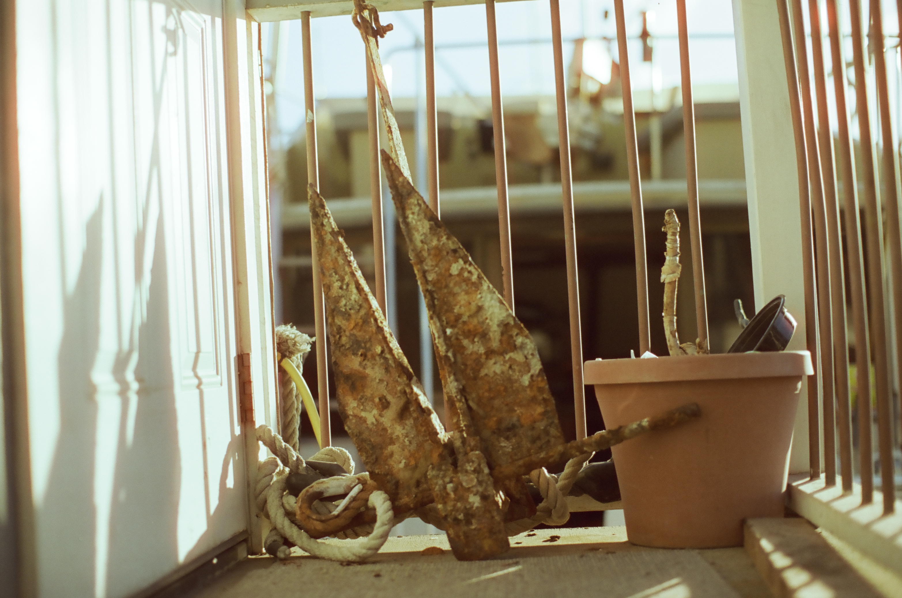 Several large rusted anchors lean beside coiled rope, a plain planter, and white vertical railings.