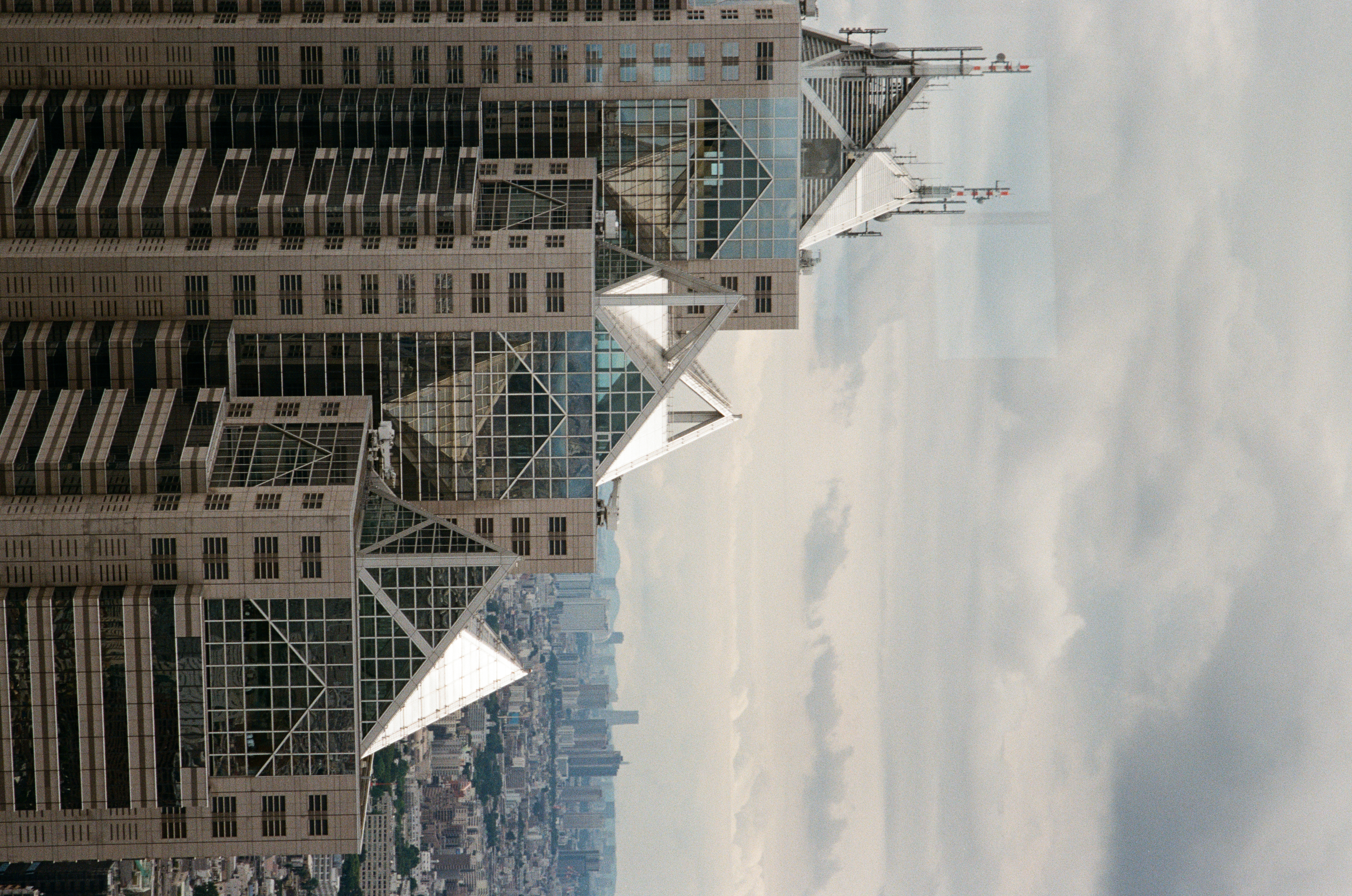 Three stepped towers with glazed pyramid roofs and antenna masts rise close against an overcast sky above a hazy, distant skyline.