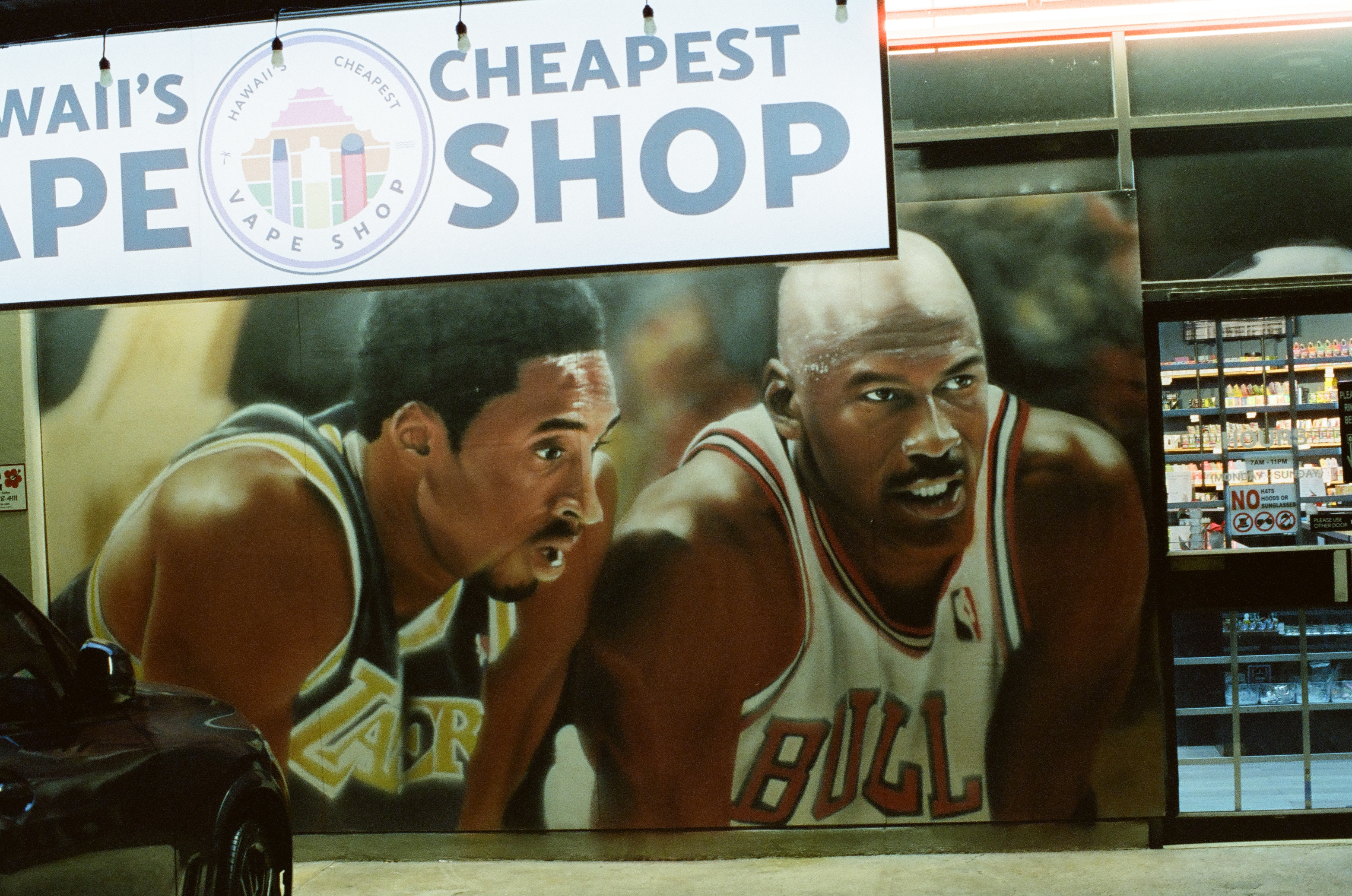 Two large painted basketball players cover a storefront wall beneath a sign advertising a vape shop.