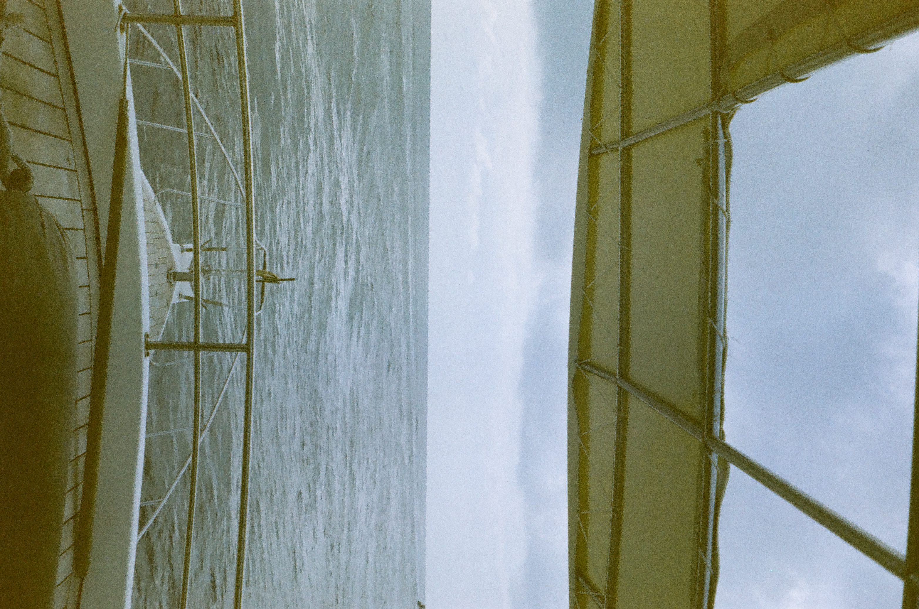 A boat canopy and railings frame open gray-blue water beneath clouds, with a cropped head at the bottom.
