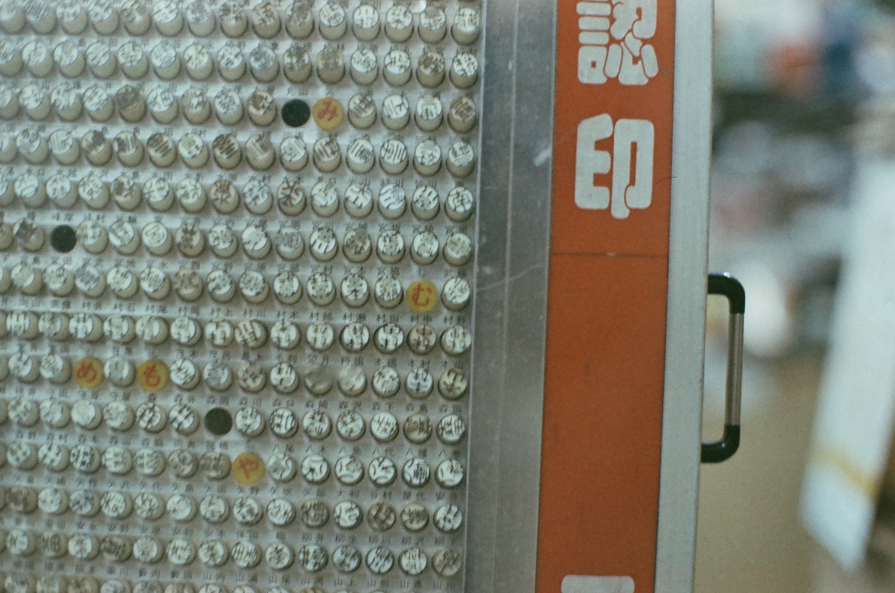 Rows of small cylindrical name-seal stamps, each capped in a clear capsule and etched with characters, fill a dense display rack.