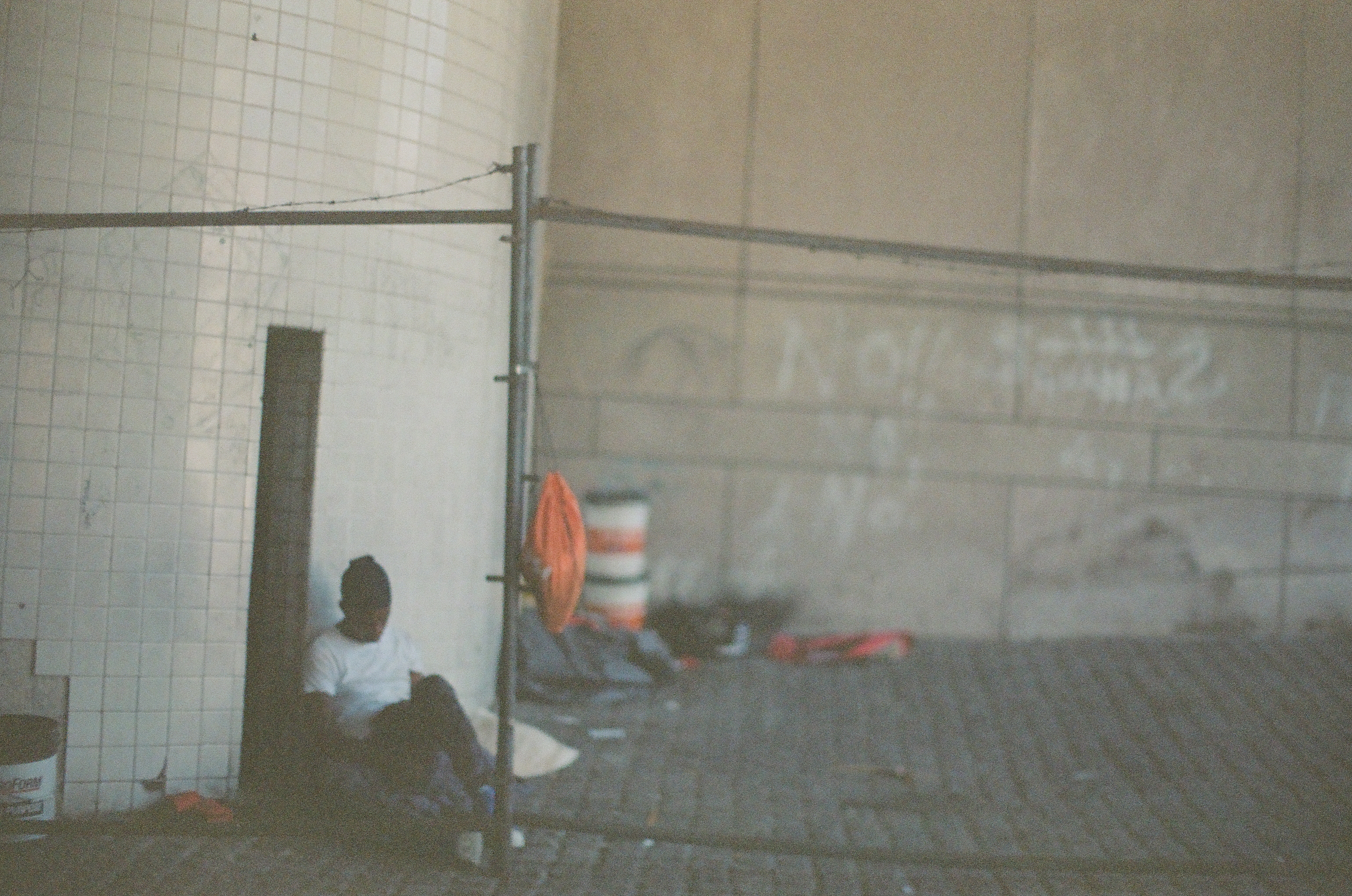 A seated person appears behind wire fencing inside a pale unfinished space with scattered materials.