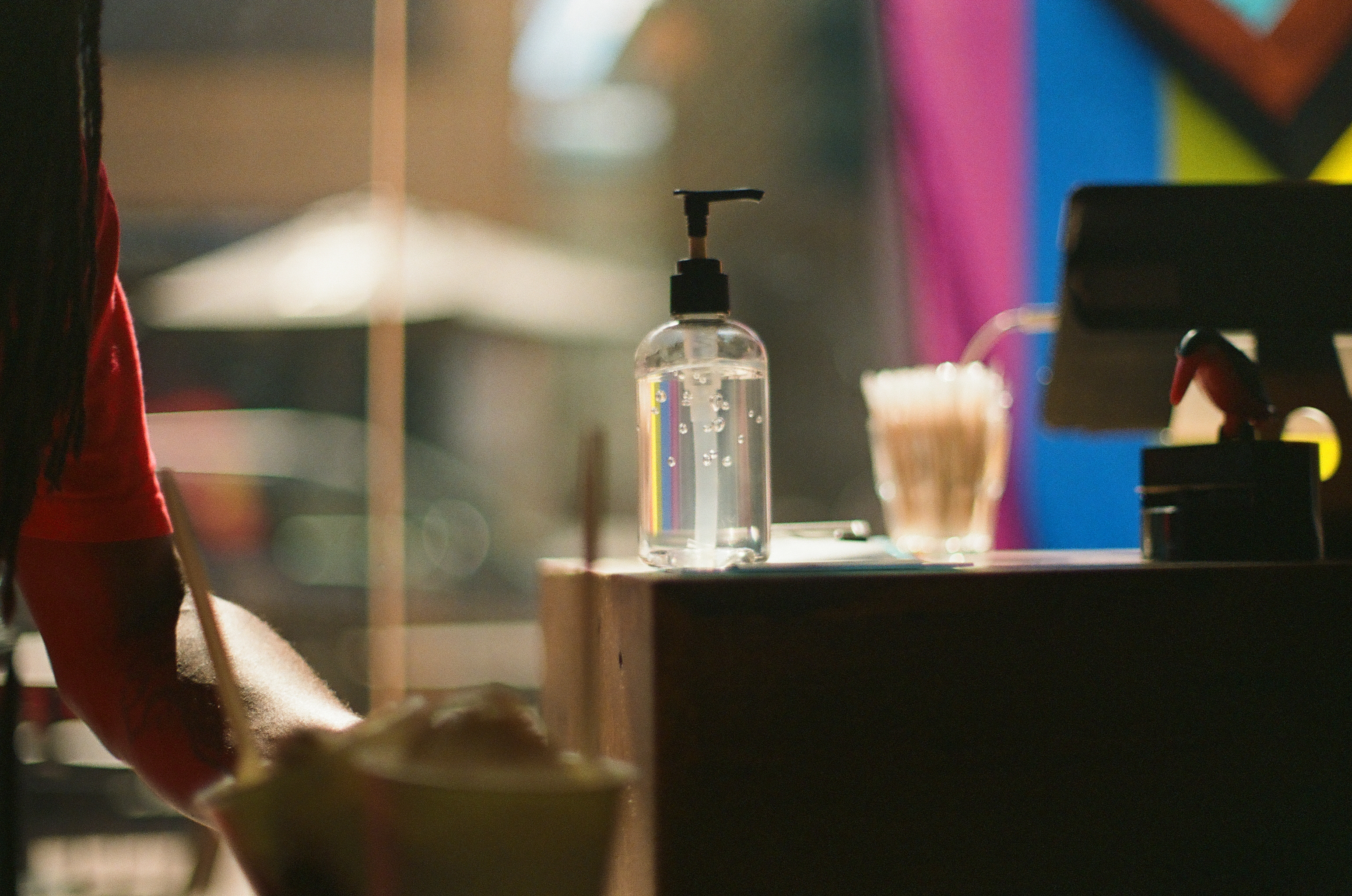 A clear pump bottle and drinking glass stand on a dark counter before soft blocks of color.