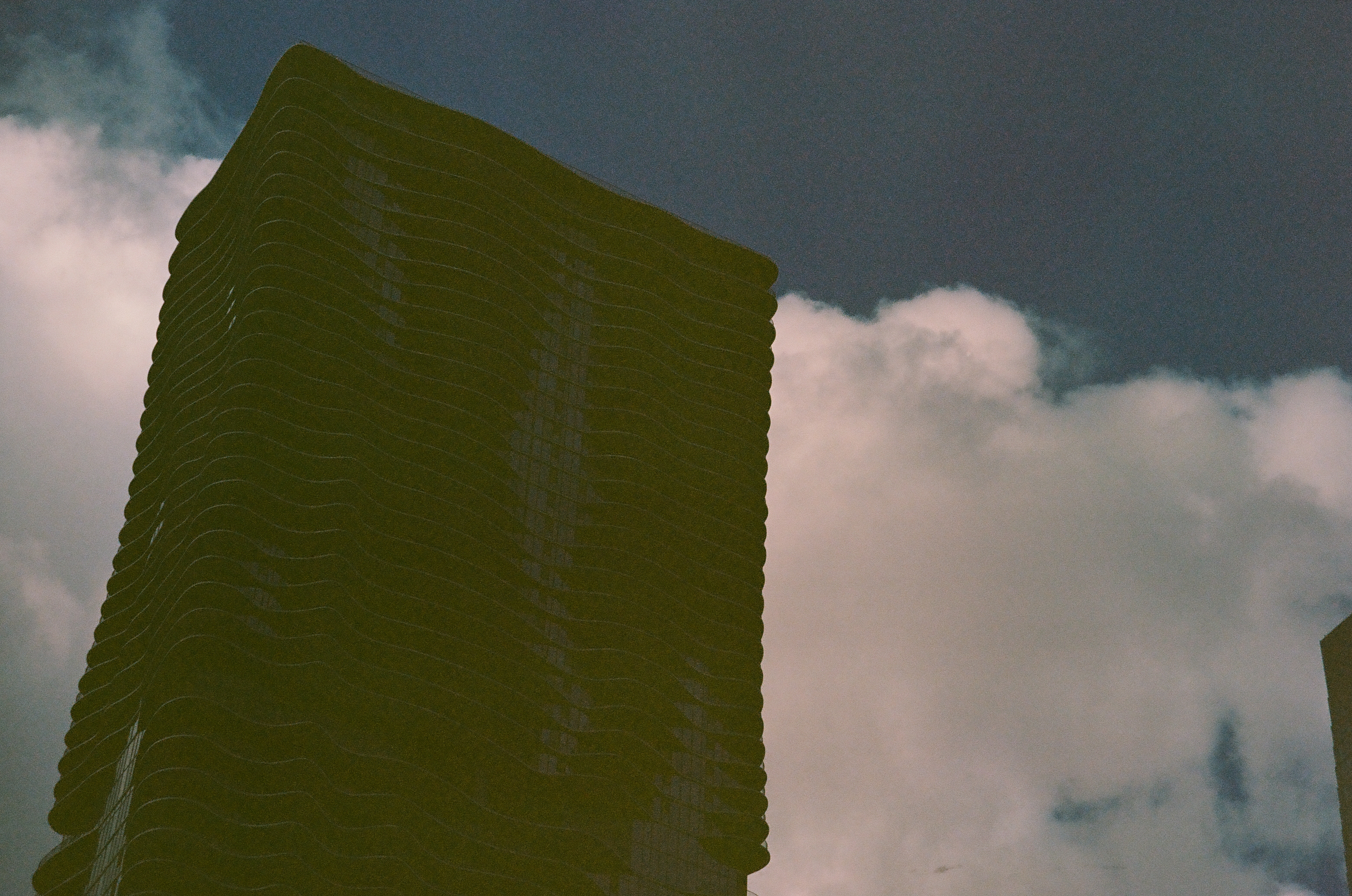 A dark ribbed high-rise fills the frame while rounded white clouds gather behind its upper edge.