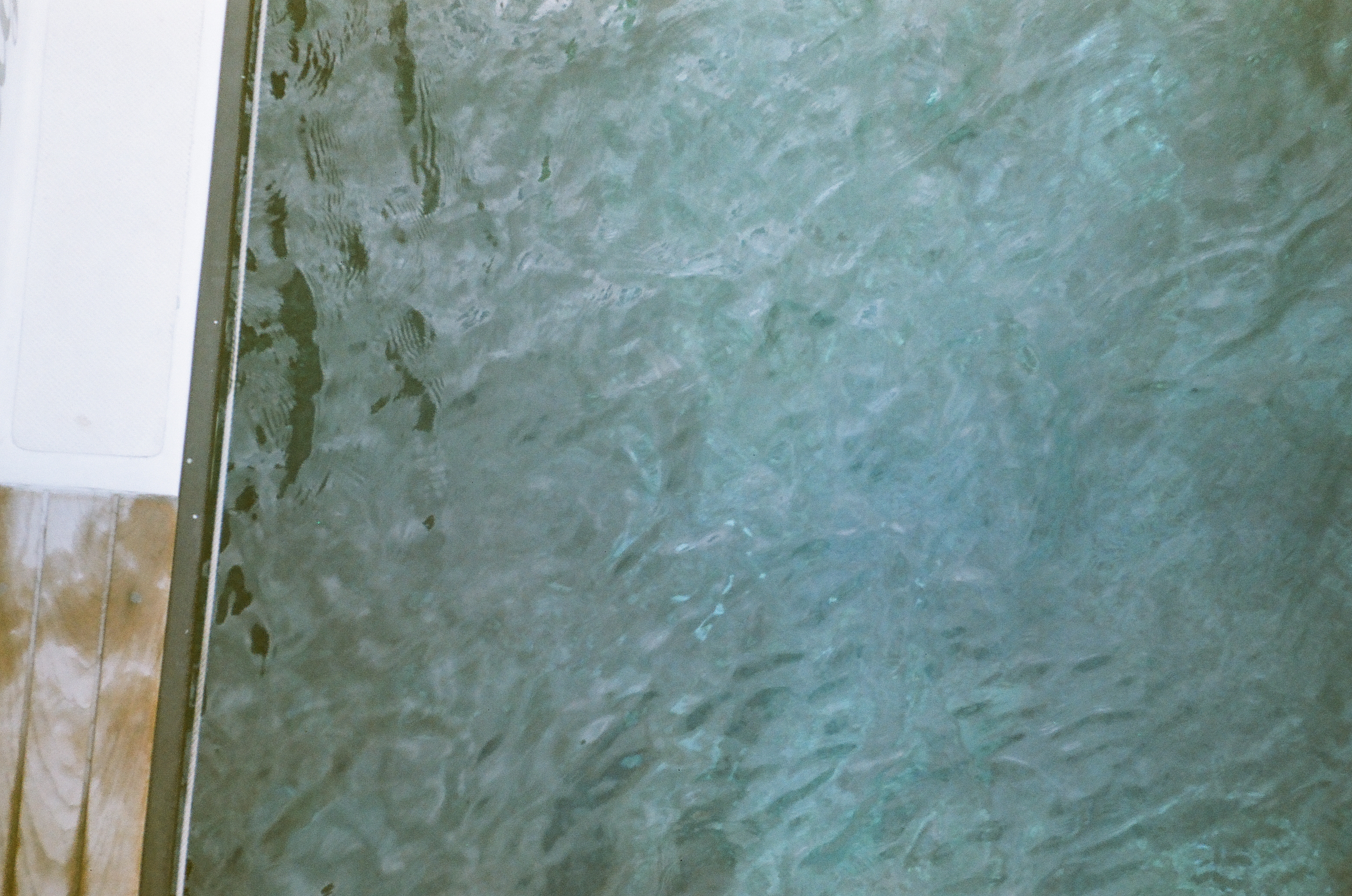 Bright turquoise water churns beside a white hull edge, filling the frame with bubbles, ripples, and wake.