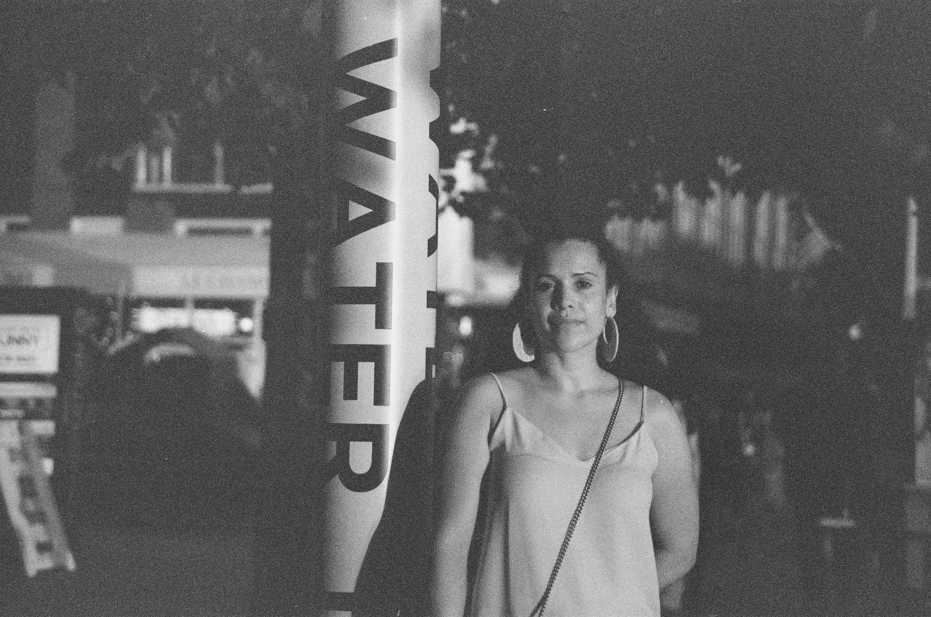 Two people face forward in monochrome light between tall vertical letters, with shelves and signs softened behind them.