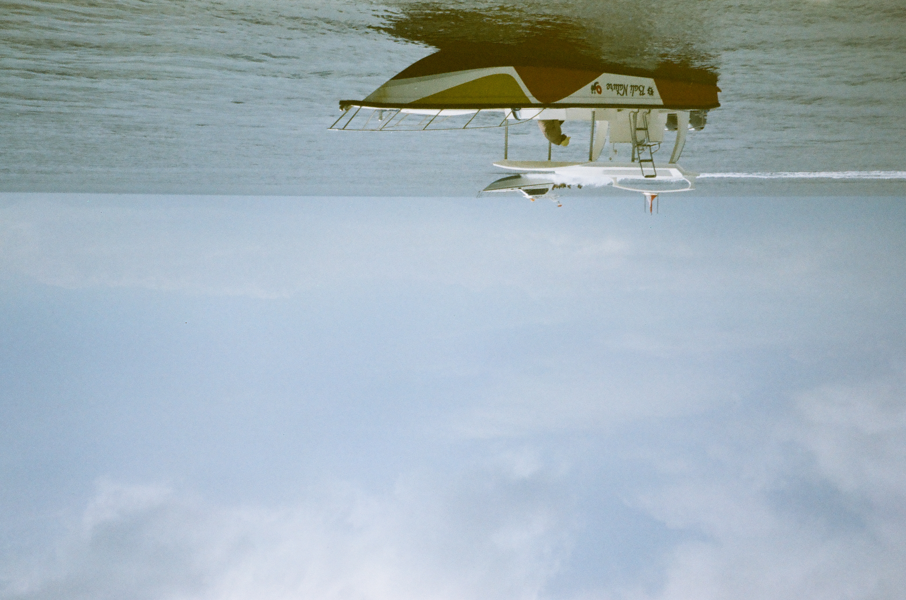 A small white motorboat carrying several people travels across calm water beneath a wide pale sky.