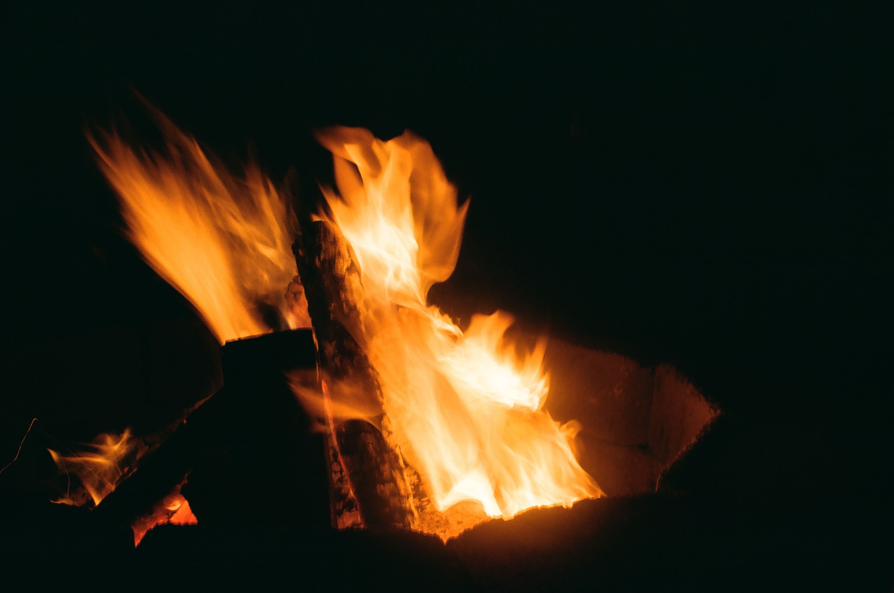Long-exposure motion blur smears flames sideways over crossed logs, their edges lit copper where the fire has not yet reached.