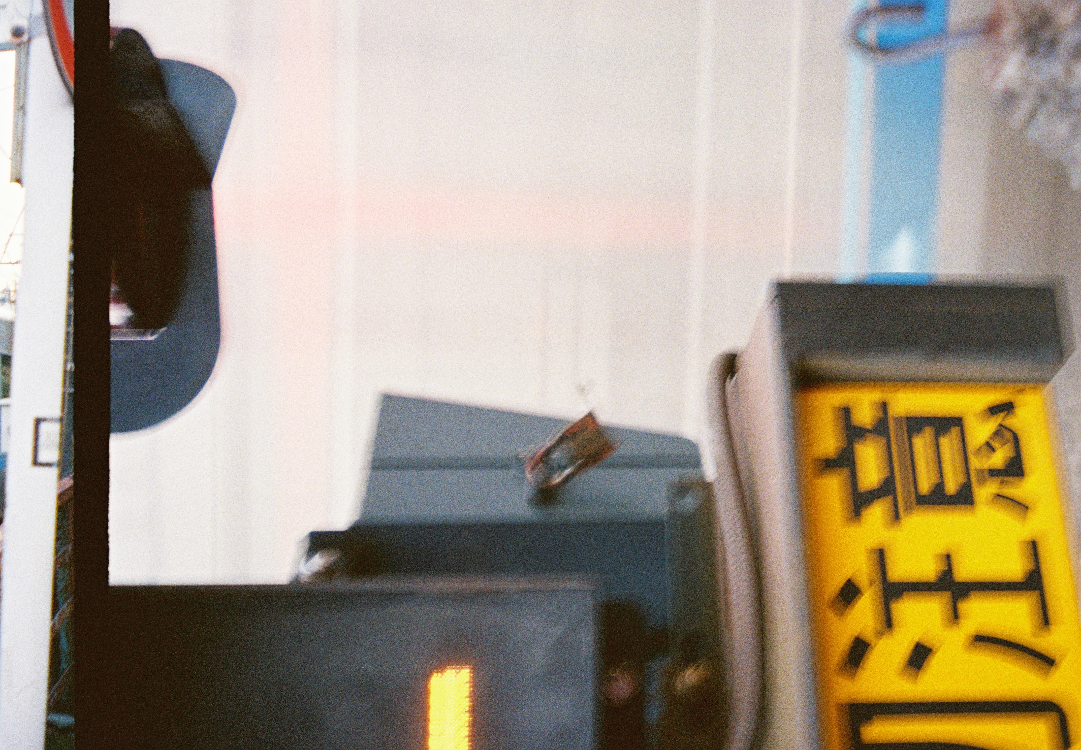 A dark signal housing with a lit amber bar sits above a yellow sign reading 注意, while a pale train blurs past behind it.