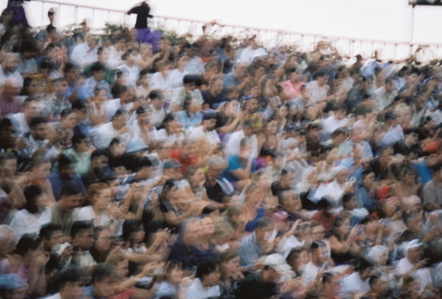 A large seated crowd stretches across the frame as lateral camera movement turns faces and clothing into soft horizontal streaks.