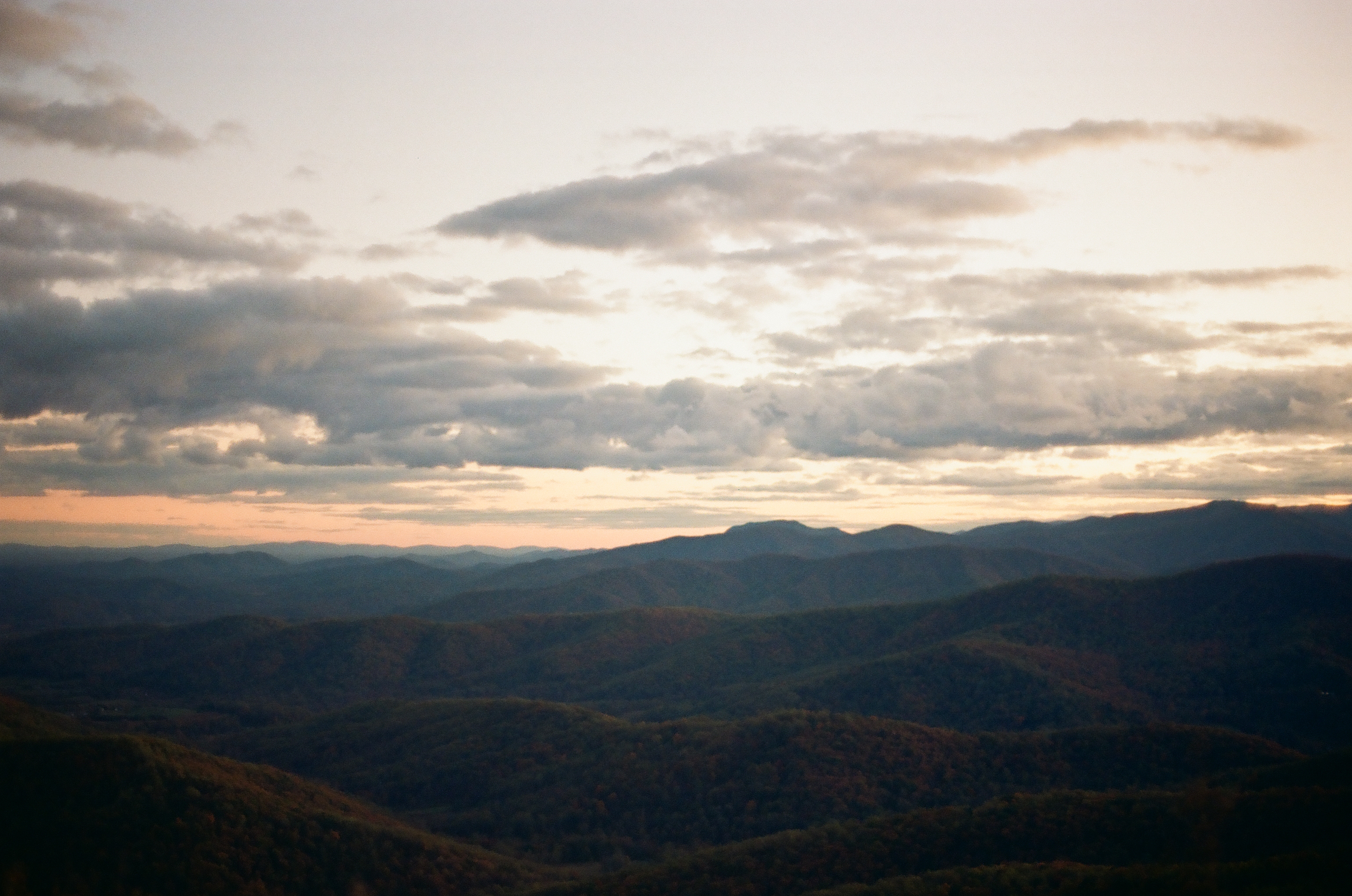 Overlapping mountain ridges recede into paler blue tones beneath a band of peach light near the horizon.