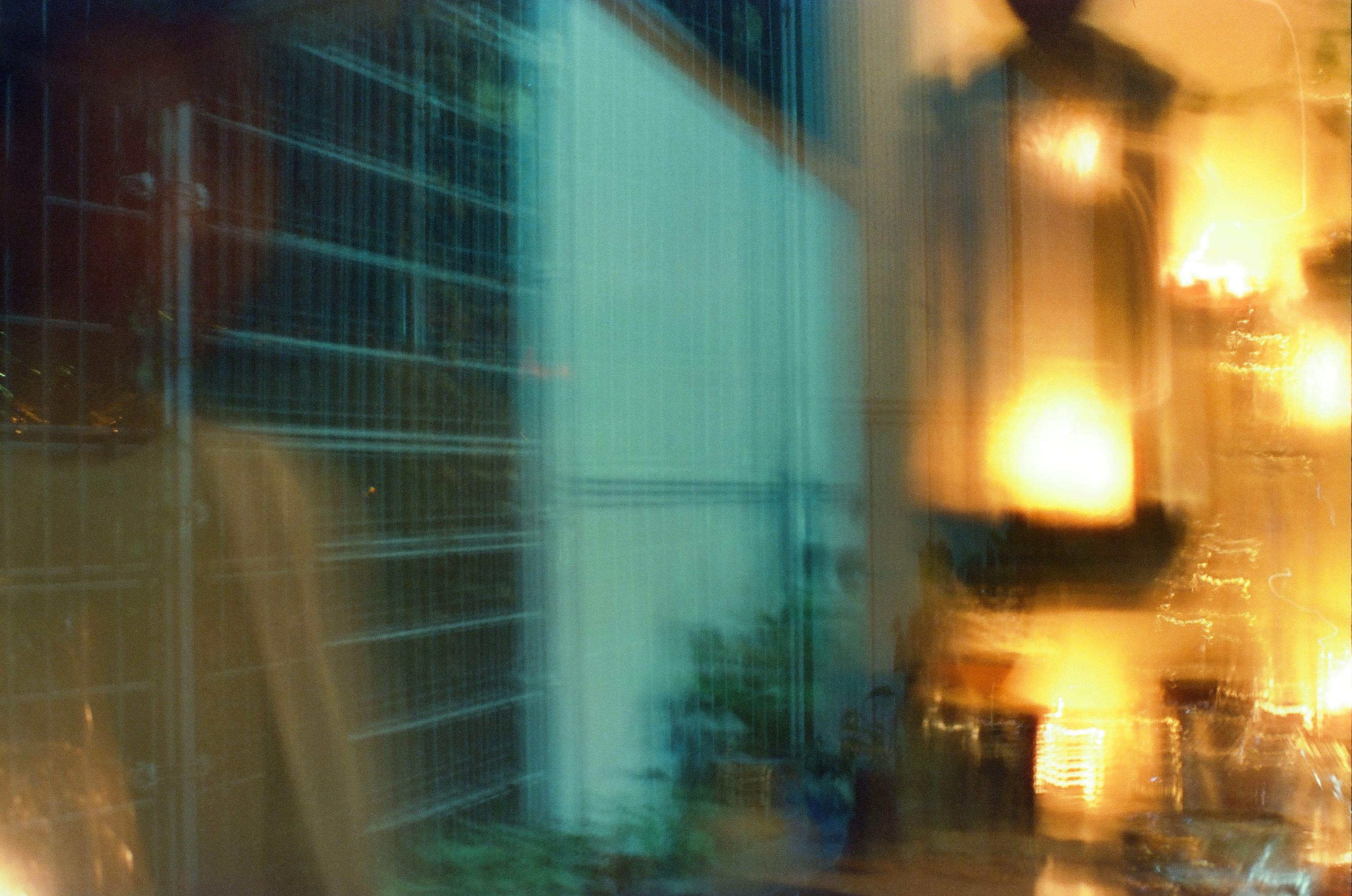 Cyan window grids and amber interior lights smear horizontally across a dark reflective glass surface.