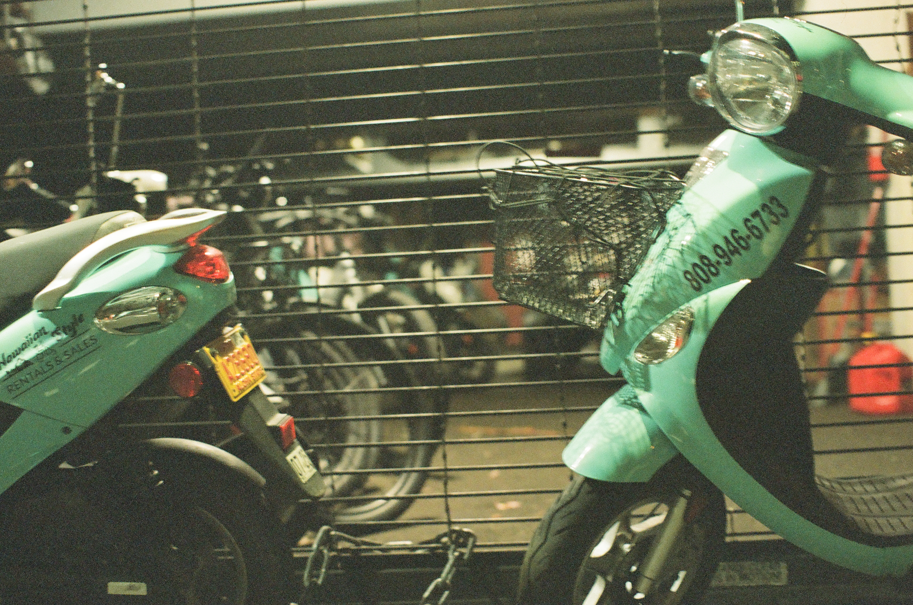 Two mint-green scooters stand before a dark metal shop shutter beneath hard nighttime light.