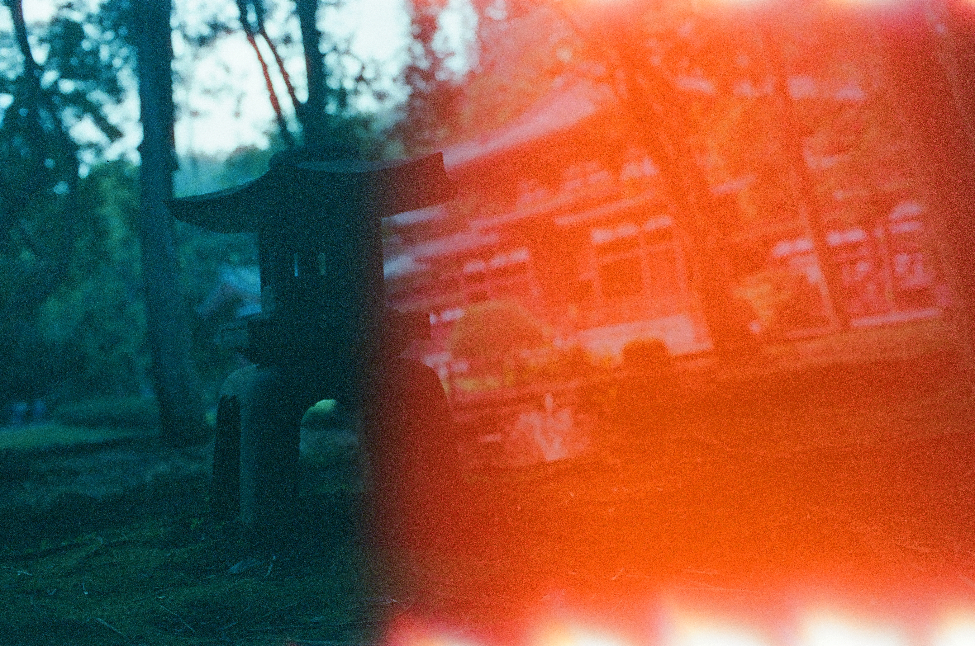 A stone lantern with a peaked cap sits among trees on the left, while red light overexposes the right half of the frame into a solid orange field.