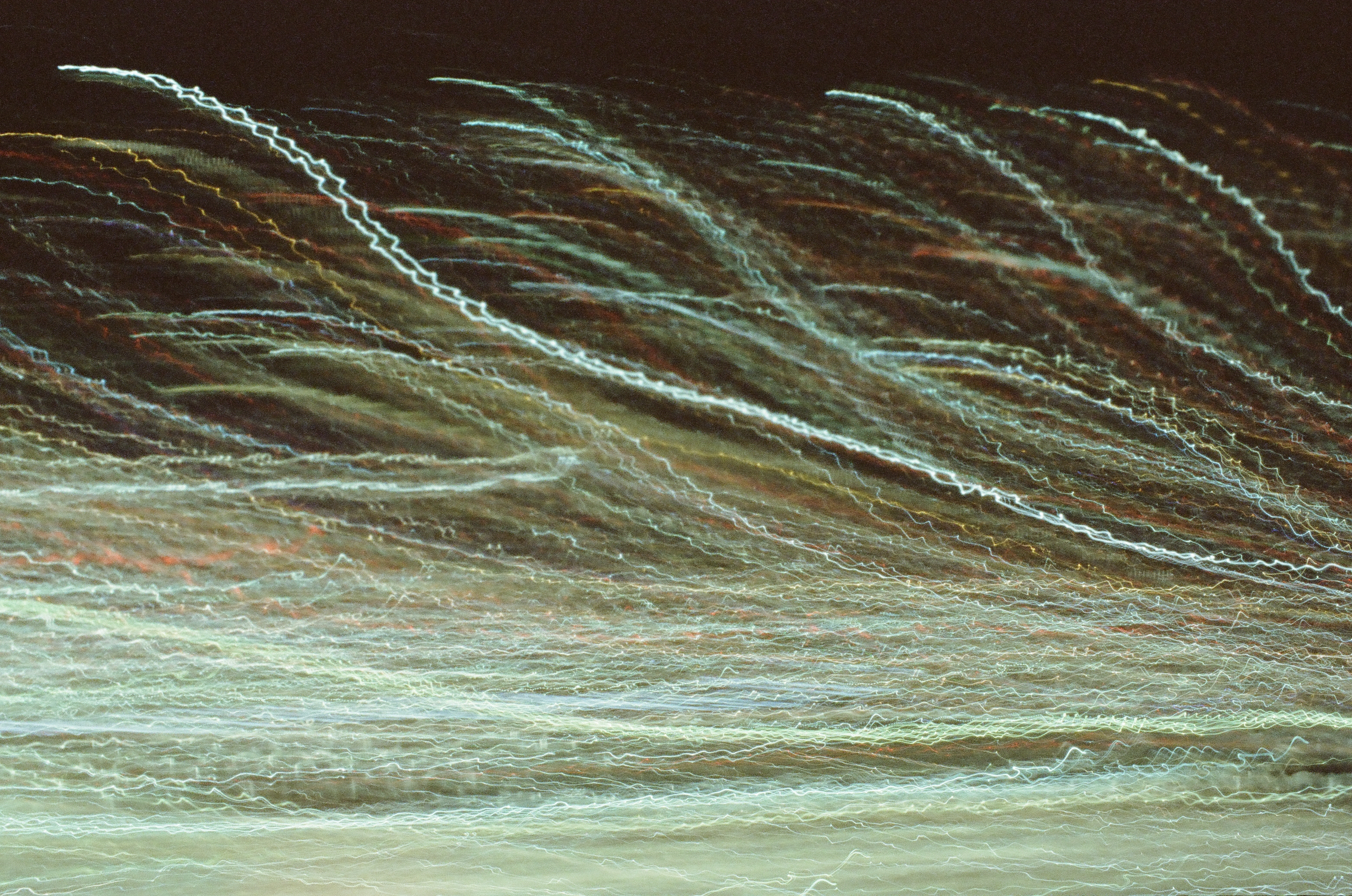 Many pale light trails sweep diagonally across a dark reddish background in loose parallel bands.