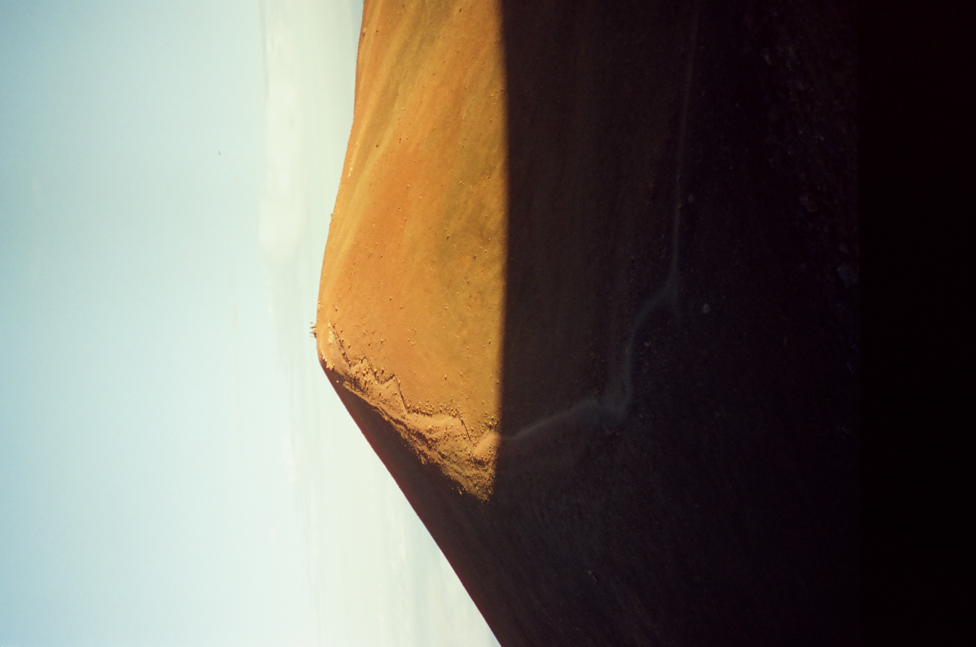 A rounded rust-colored volcanic cone rises from deep shadow beneath a clean pale blue sky.