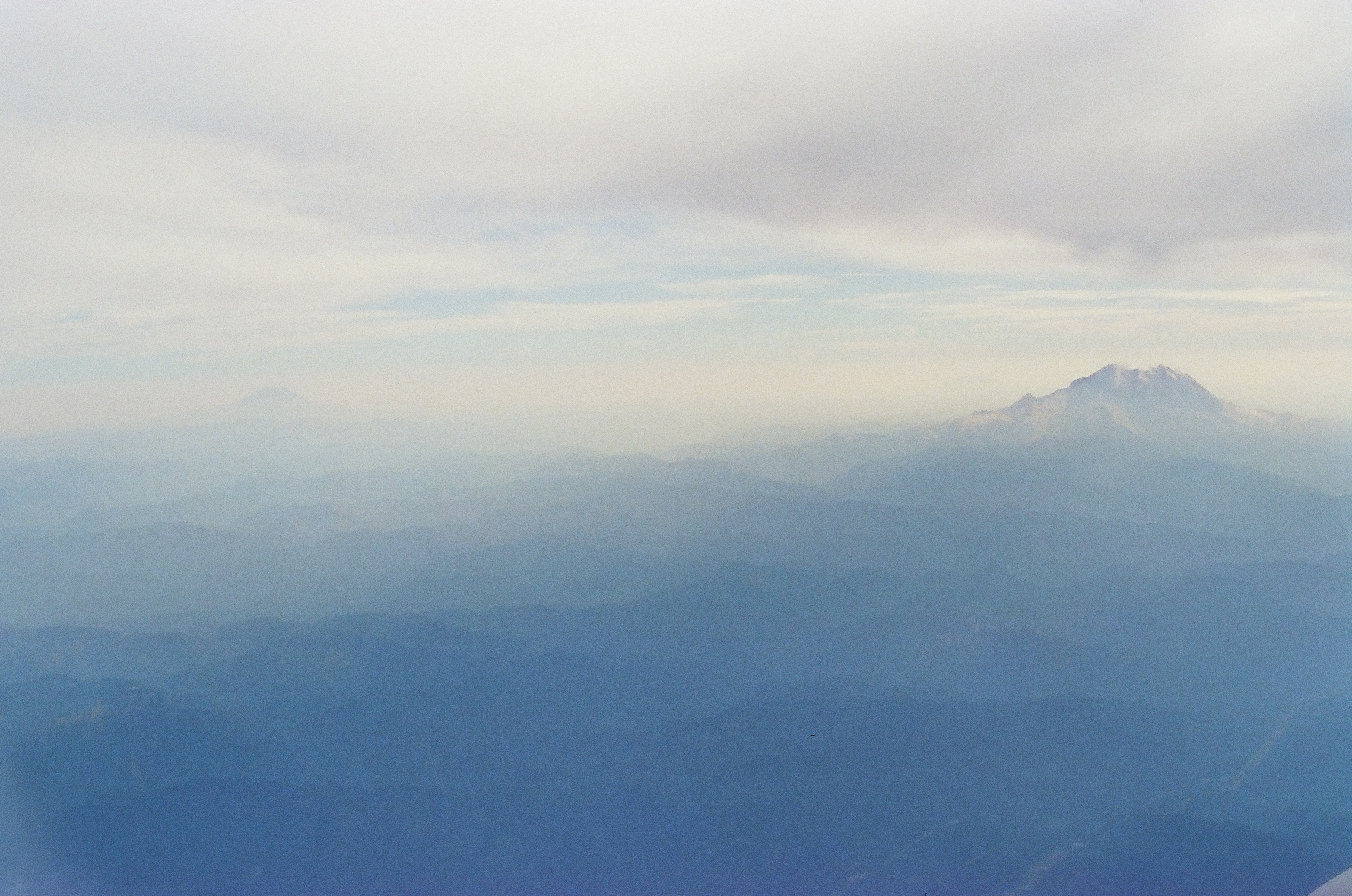 Two mountain peaks are visible above hazy layered ridgelines, a smaller faint peak on the left and a larger snow-capped peak anchoring the right side of the frame.