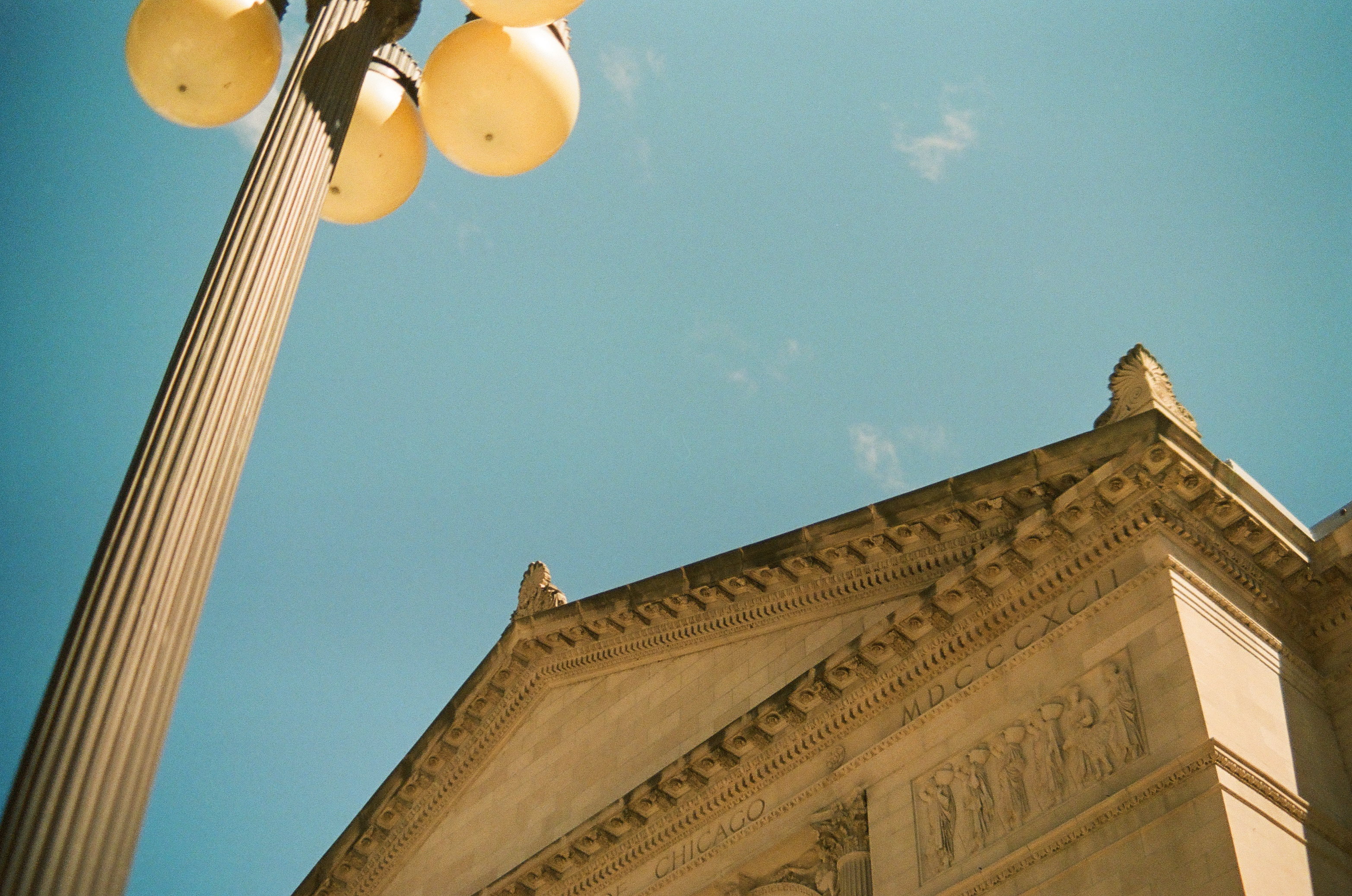 A tall globe streetlamp leans beside a carved triangular pediment under an open blue sky.