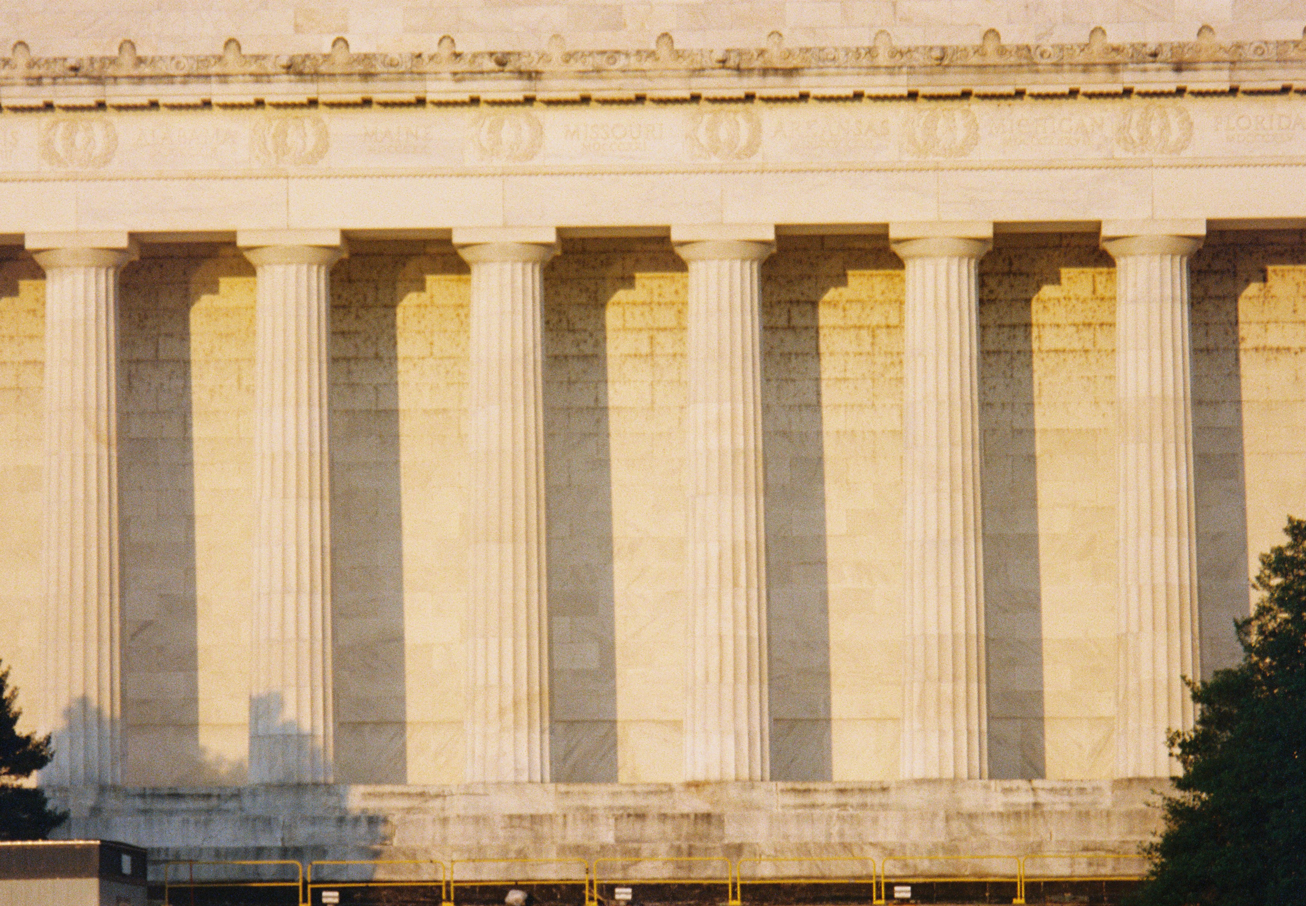Tall memorial columns repeat across a pale stone facade glowing in low warm evening sunlight.