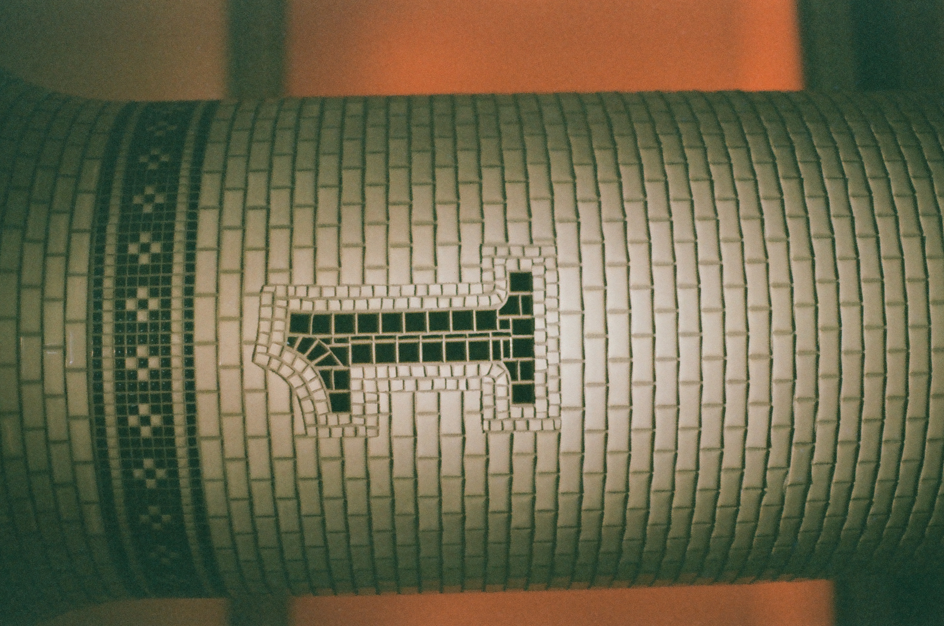 A tiled column shows the numeral one formed from dark mosaic tesserae beneath a checkered band, set against a deeply saturated blurred orange background.