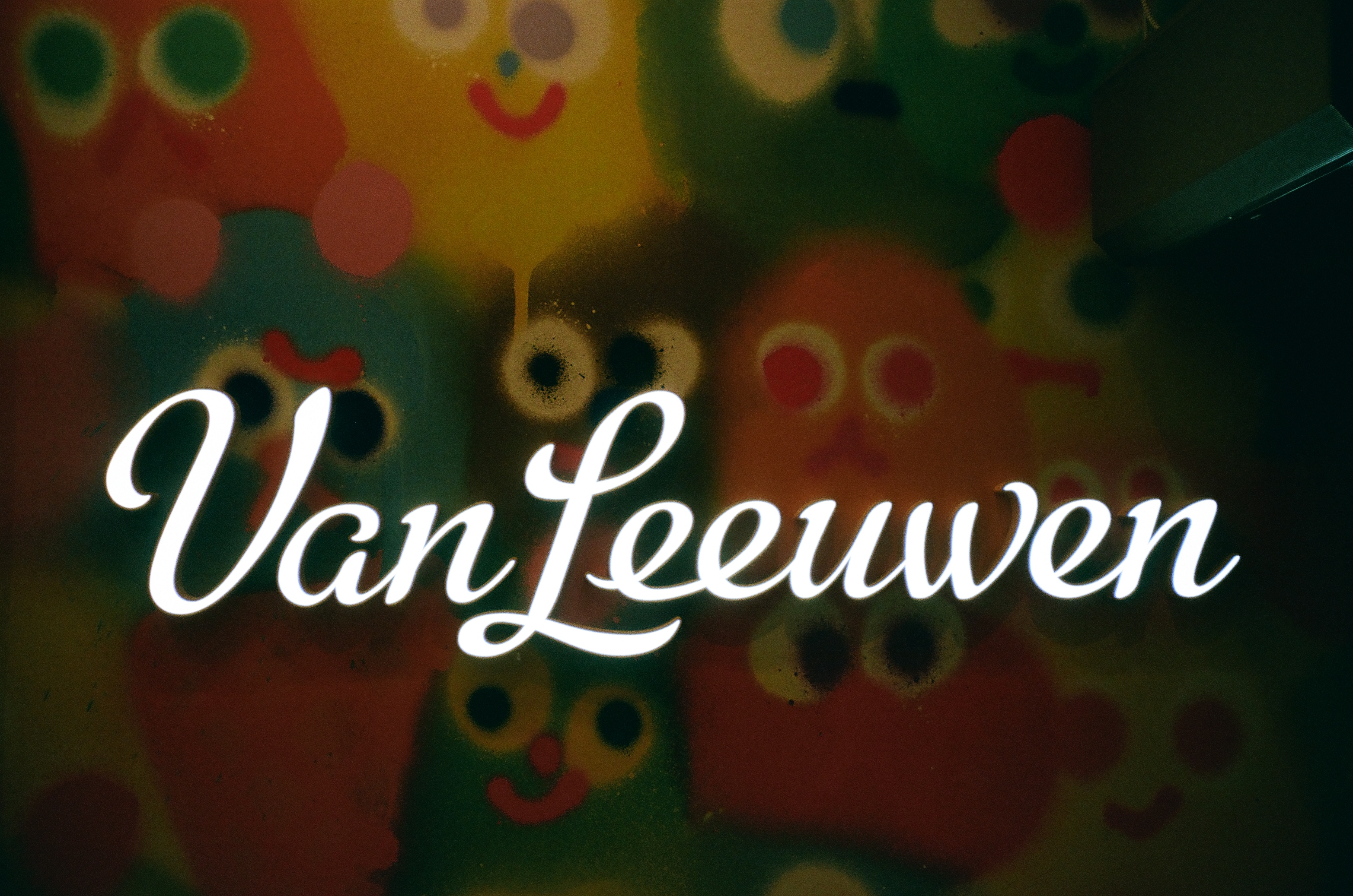 White script stretches across glass backed by colorful round figures in red, green, orange, and blue.