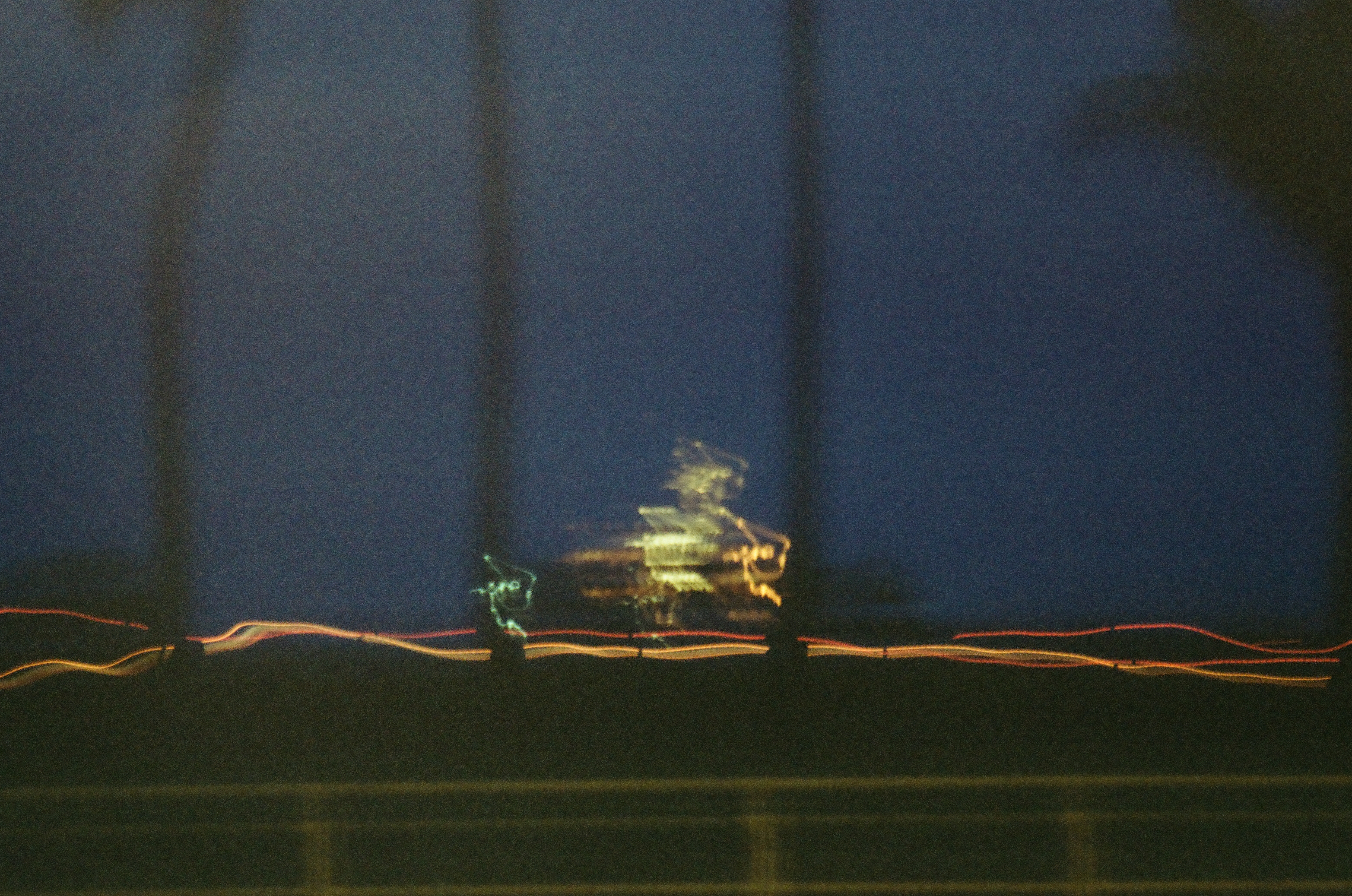 A brightly lit vessel blurs across dark water above thin orange, white, and green light trails.