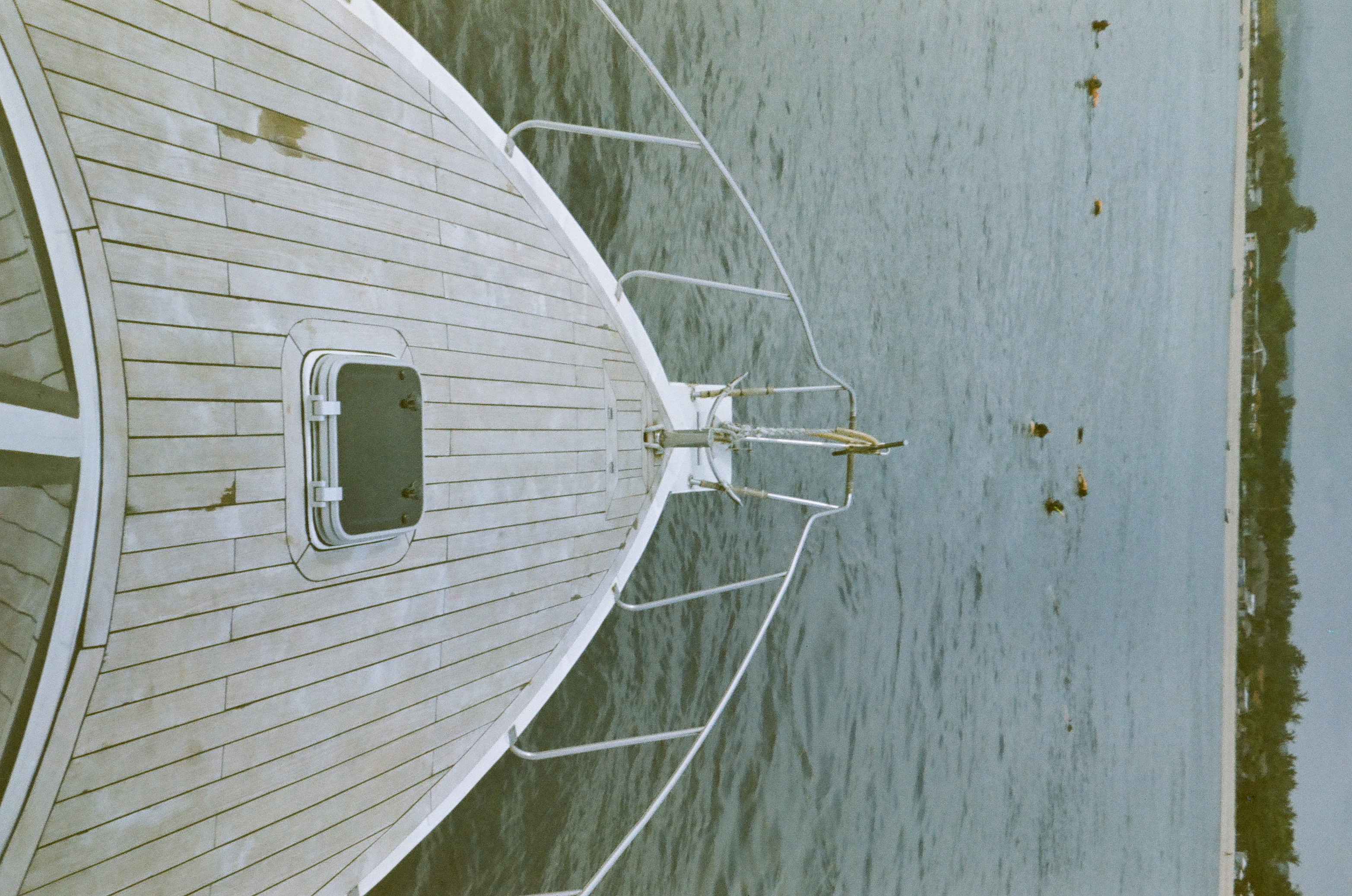 Wooden deck planks and paired rails converge toward the bow as dark buoys dot the water near shore.