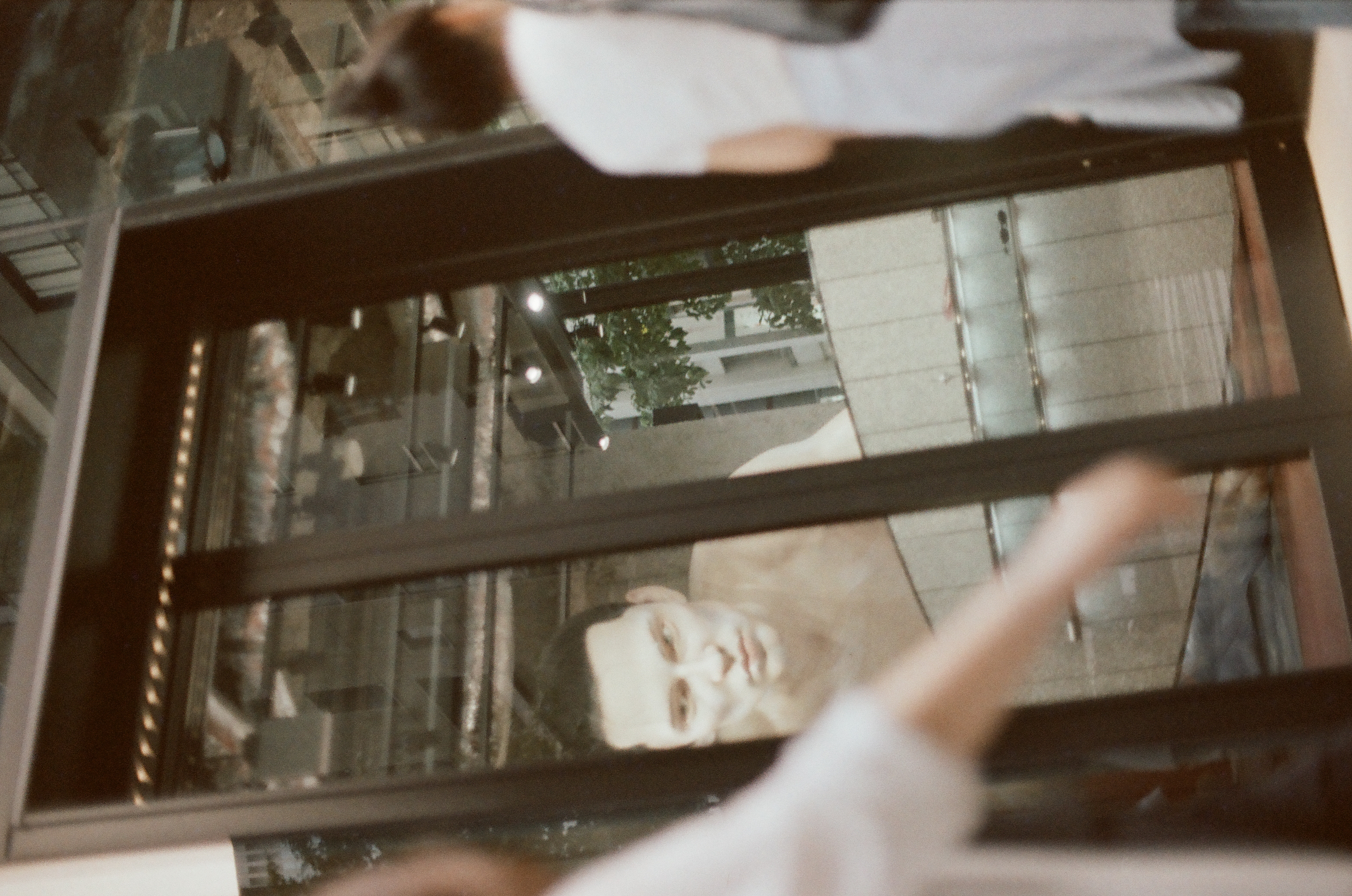 Two pedestrians in white clothing blur across the foreground of a glass storefront door showing the same large figure image behind mullions.