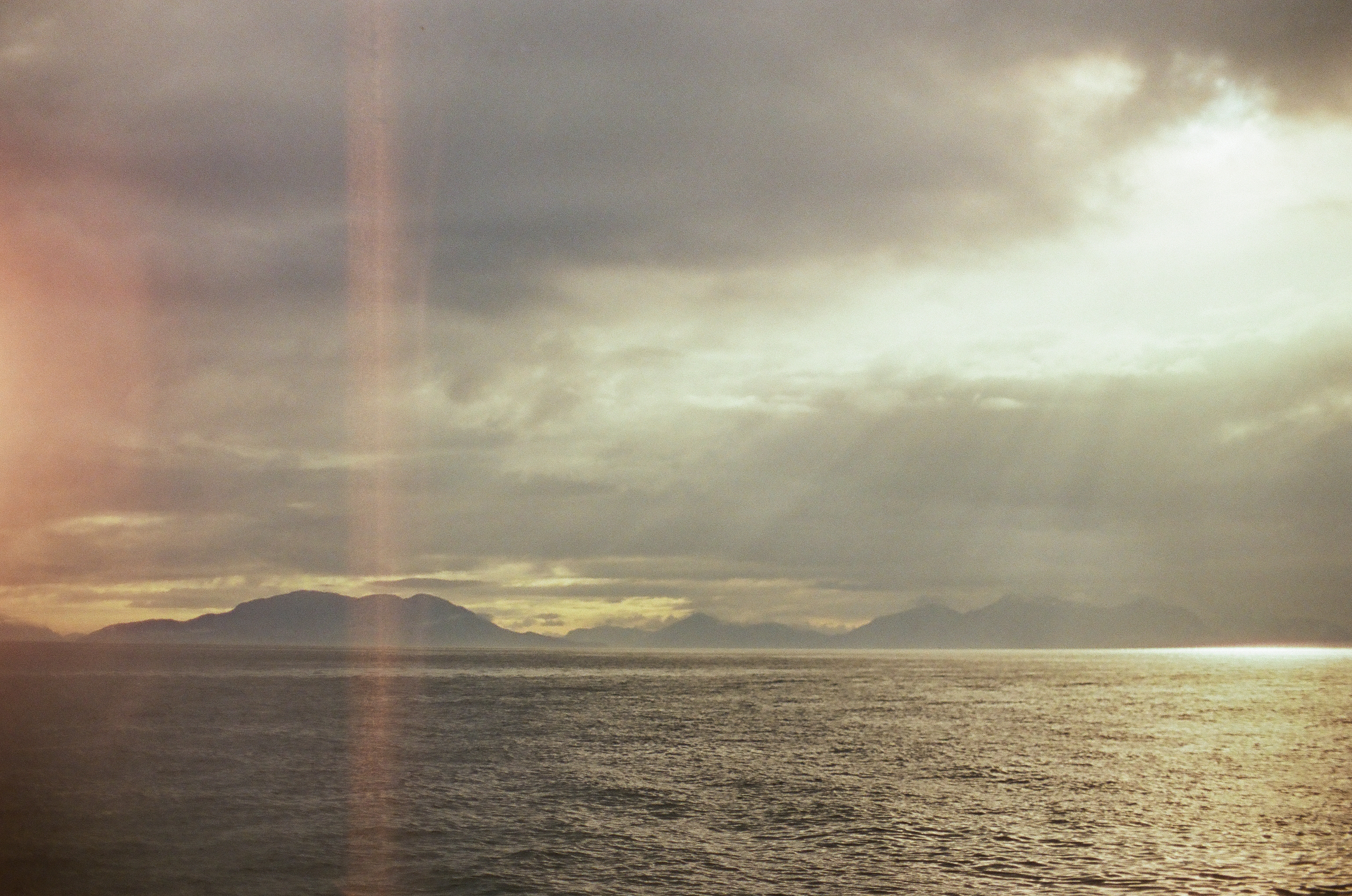 Dark mountain silhouettes line the horizon beneath layered clouds and a bright reflection across open water.