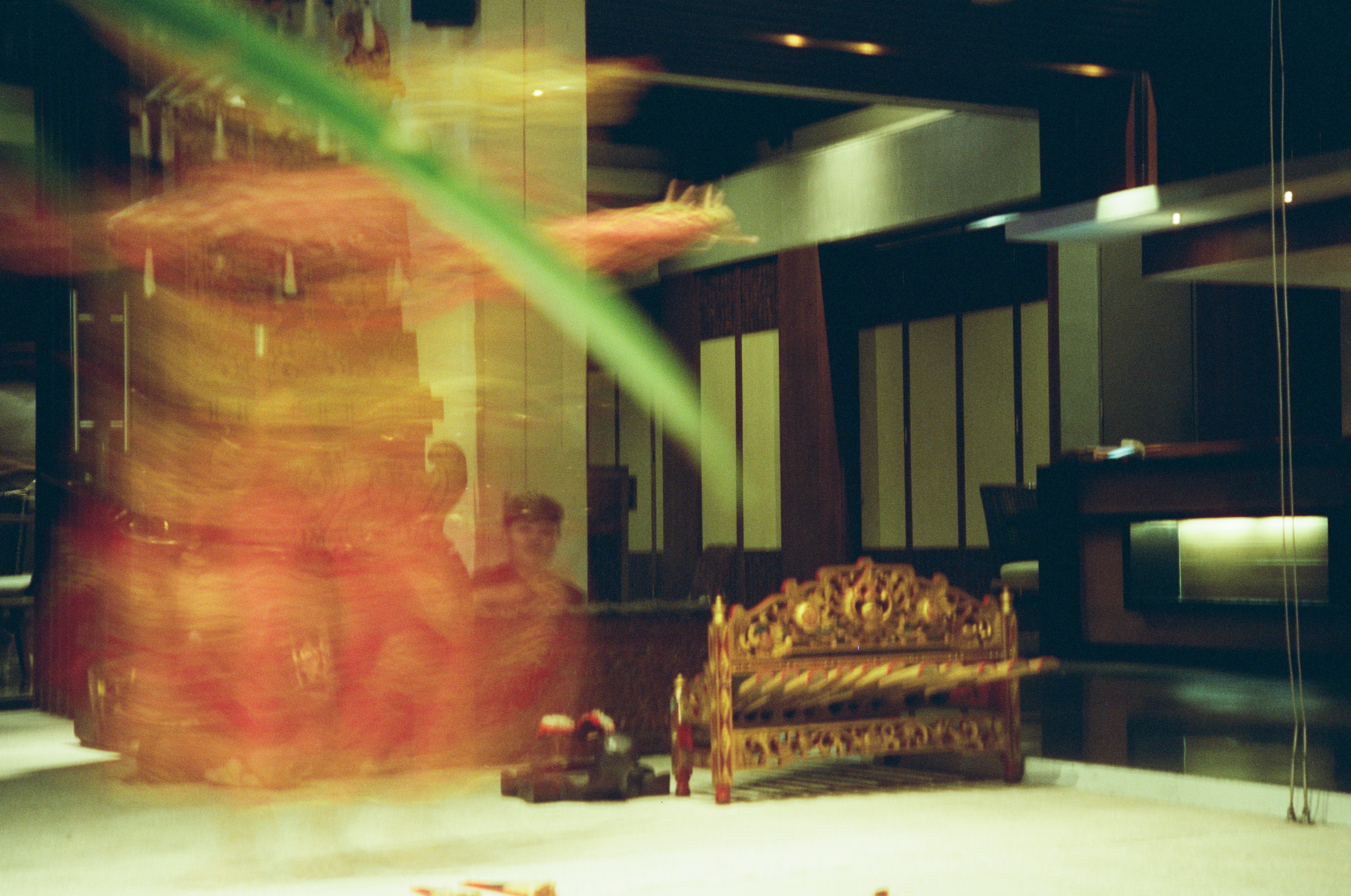 An ornate carved object with parallel bars stands on a pale floor beside a broad red blur and green diagonal.