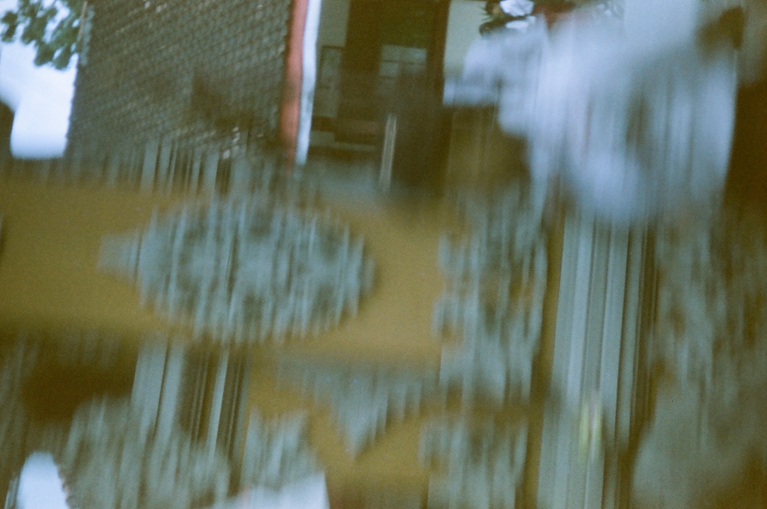 Blurred gray raised forms and an ochre wall overlap a dark tiled roof and an open building frontage.