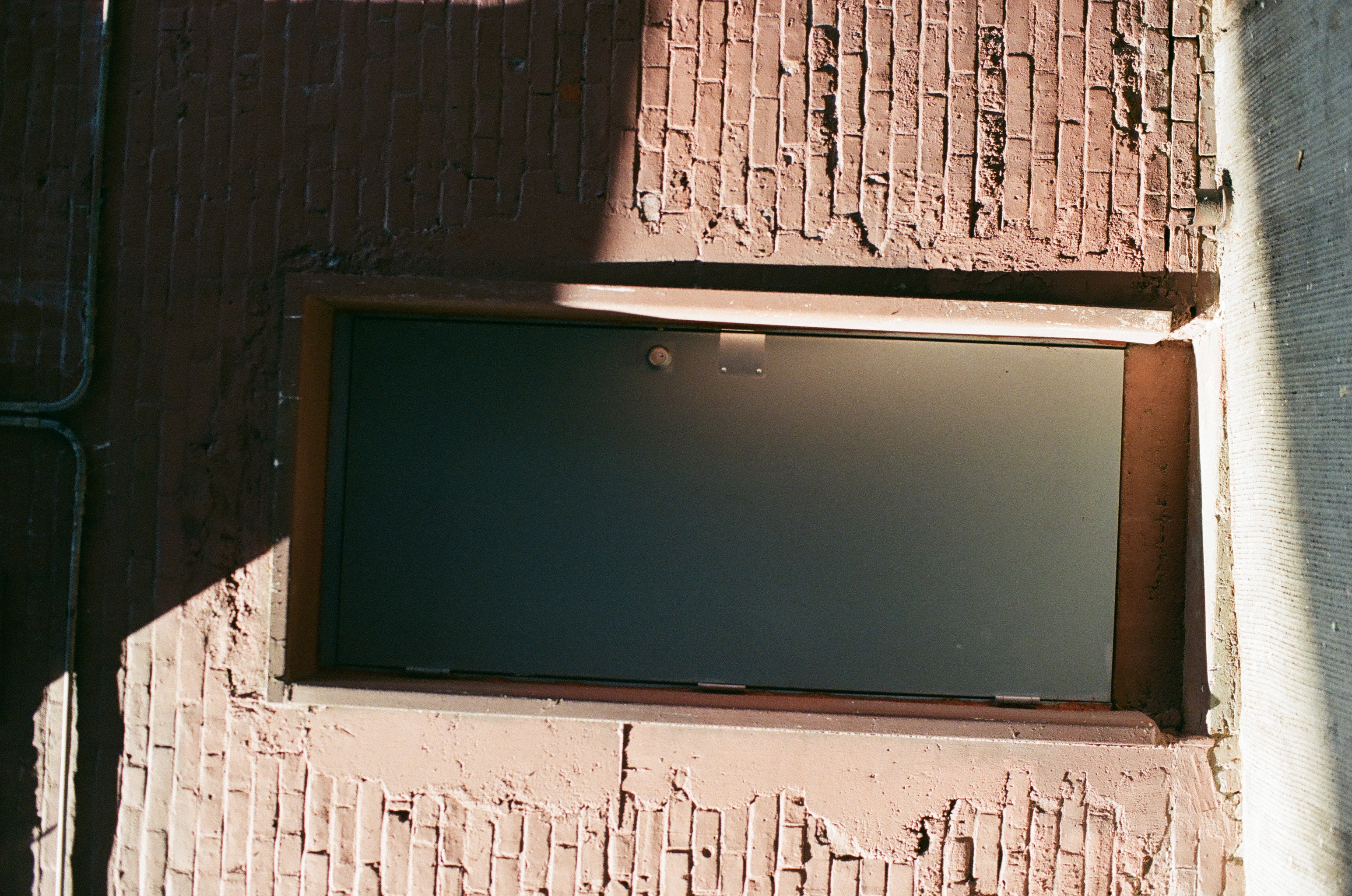 A plain gray metal door sits inside a pink brick wall beneath a thin horizontal pipe.