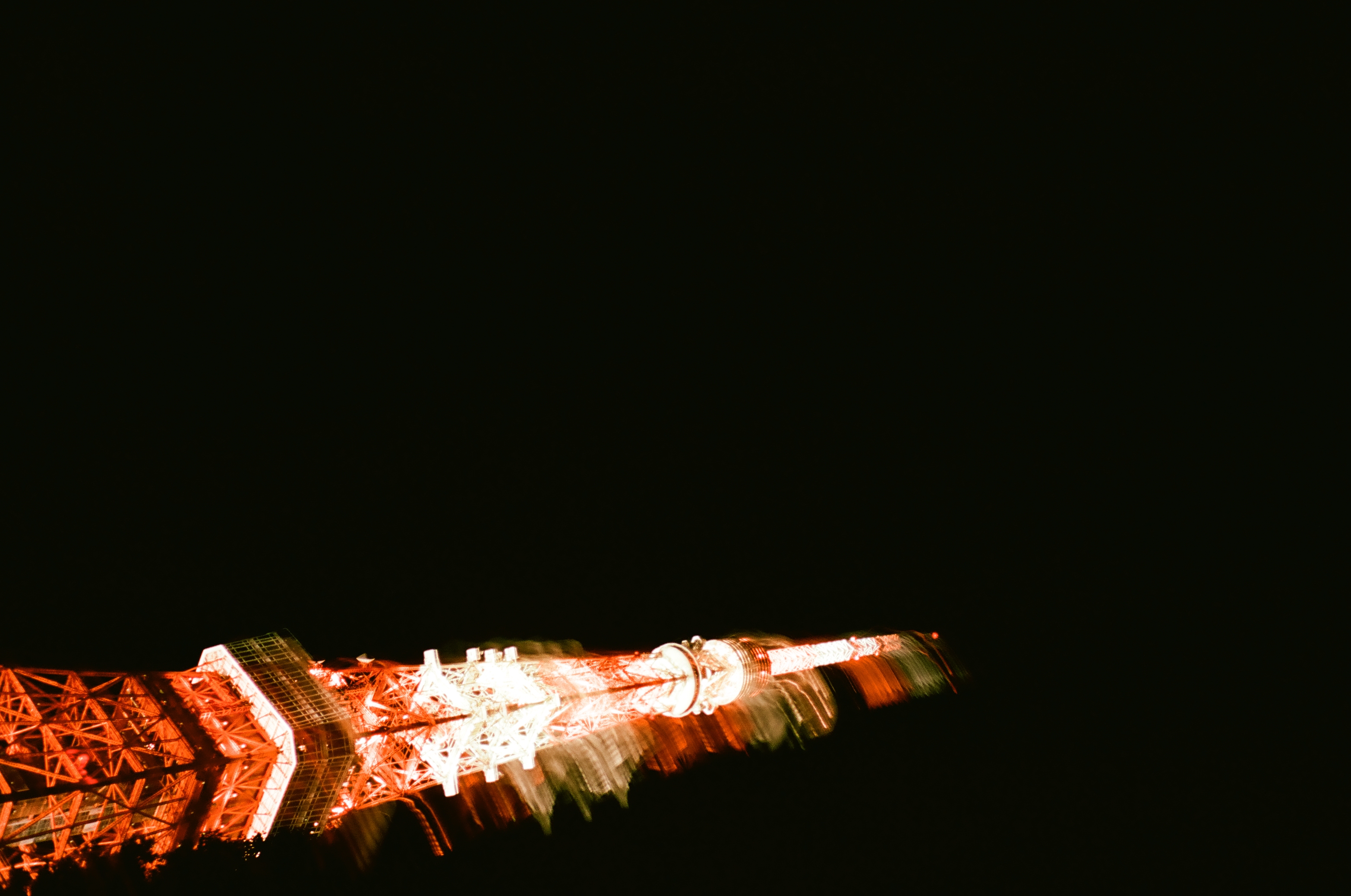 An illuminated red and white lattice tower tilts and smears horizontally across a nearly black night sky.